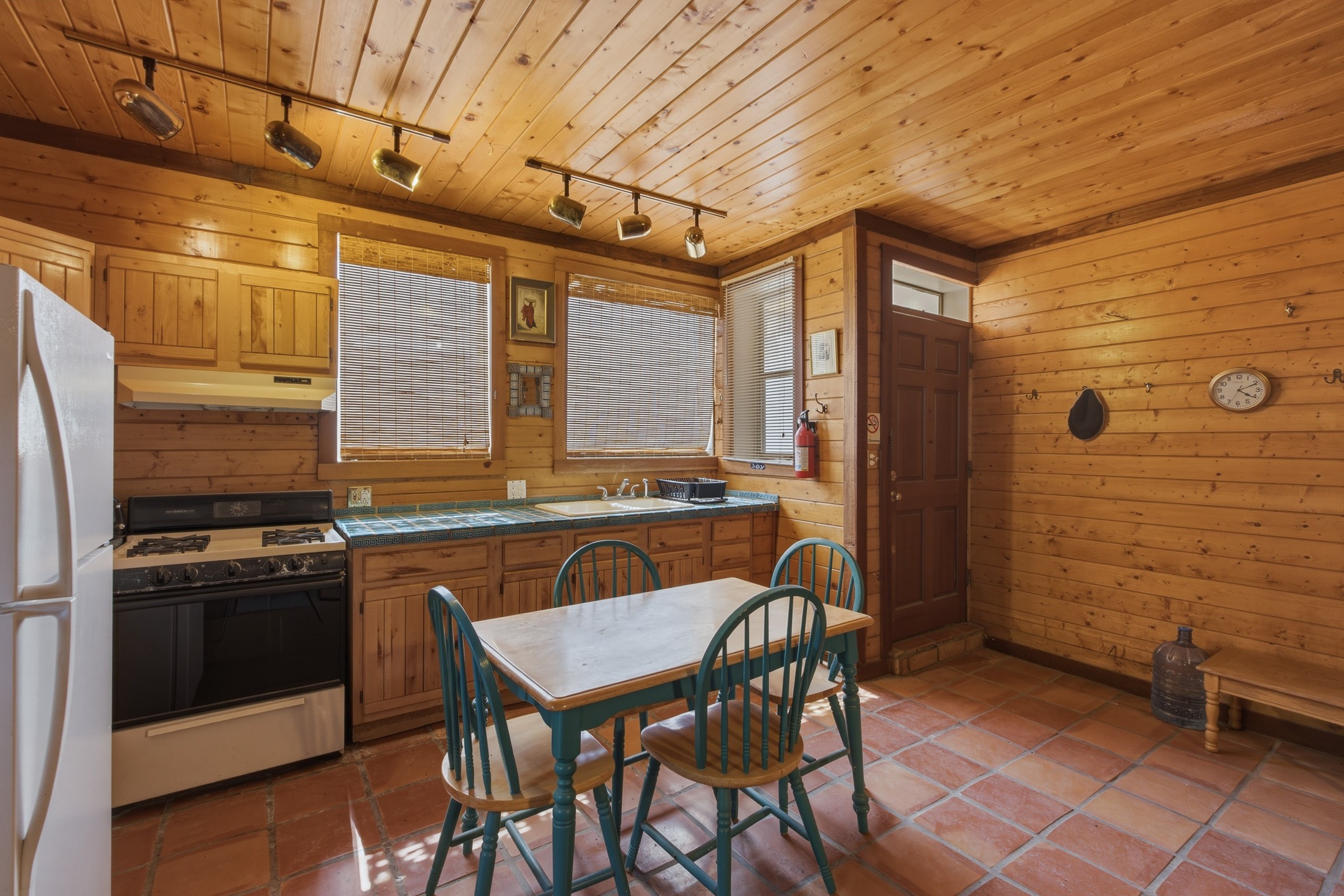 Wood-paneled kitchen with tiled counters and terracotta floors, featuring a dining table with teal chairs.