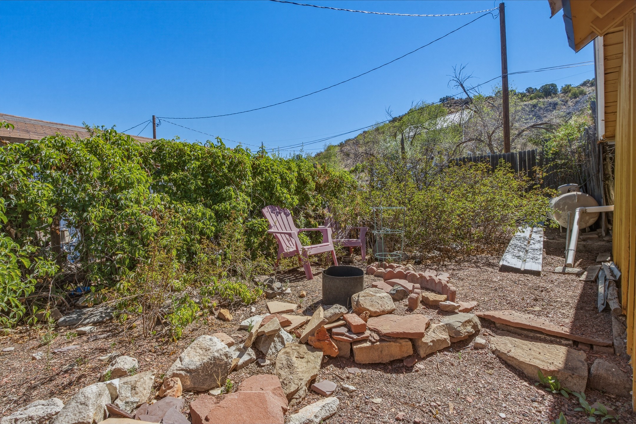 Backyard with pink Adirondack chairs, gravel landscaping, shrubs, and a stone fire pit area.