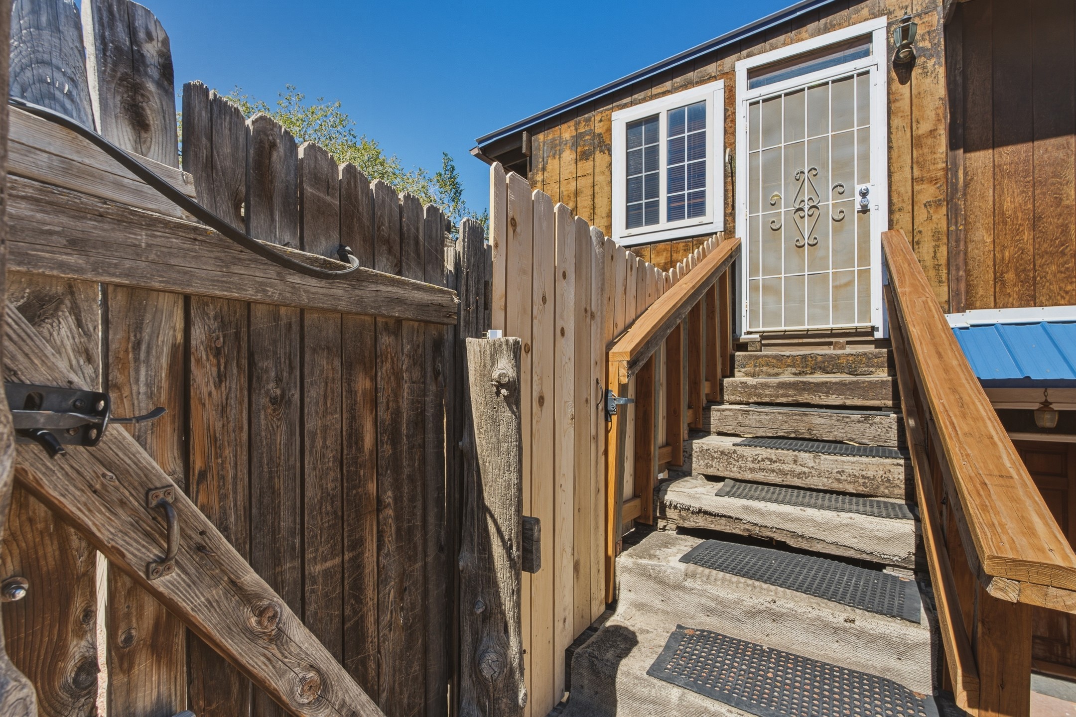 Wooden steps with traction mats lead to a white security door beside a rustic fenced entry.