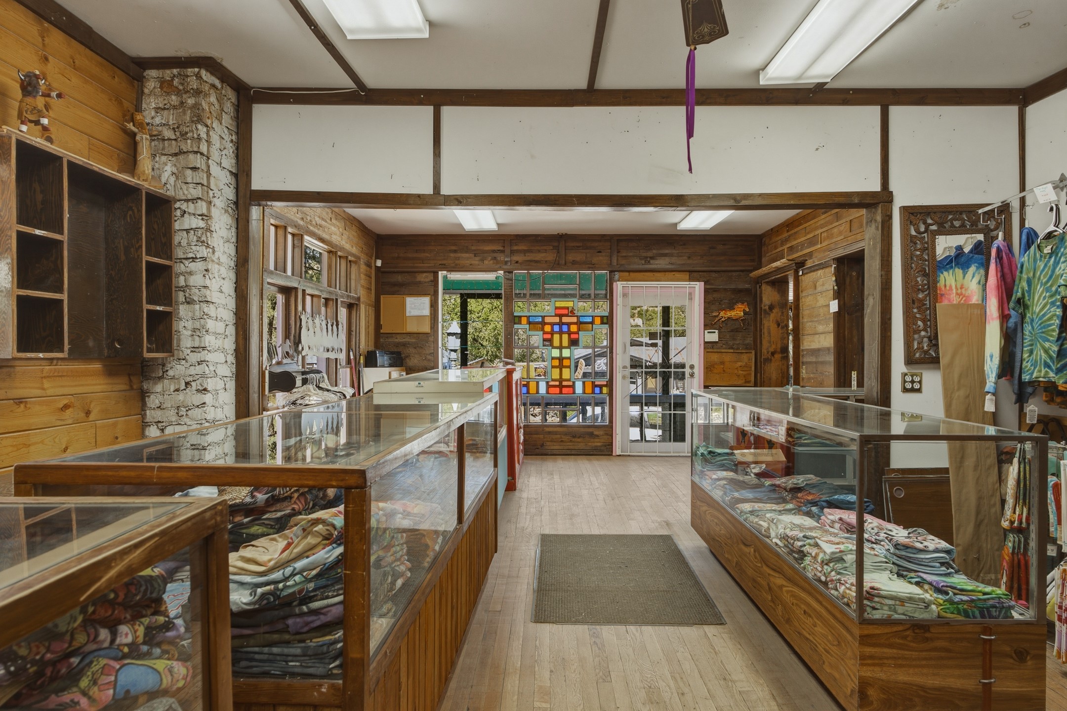 Rustic shop interior with glass display counters of folded textiles and colorful stained-glass panels.