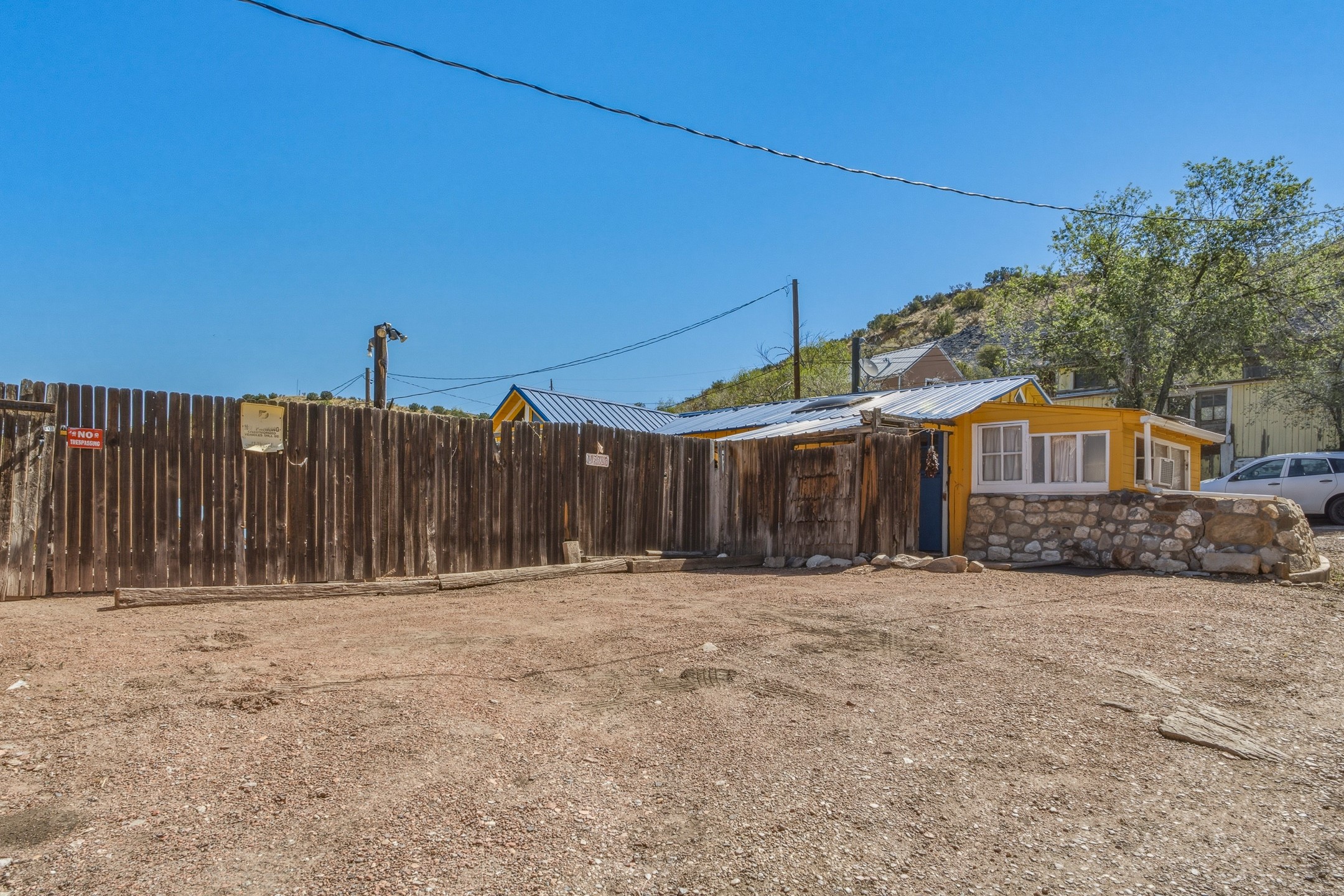Yellow house behind a wooden fence and stone wall, with a wide gravel yard.