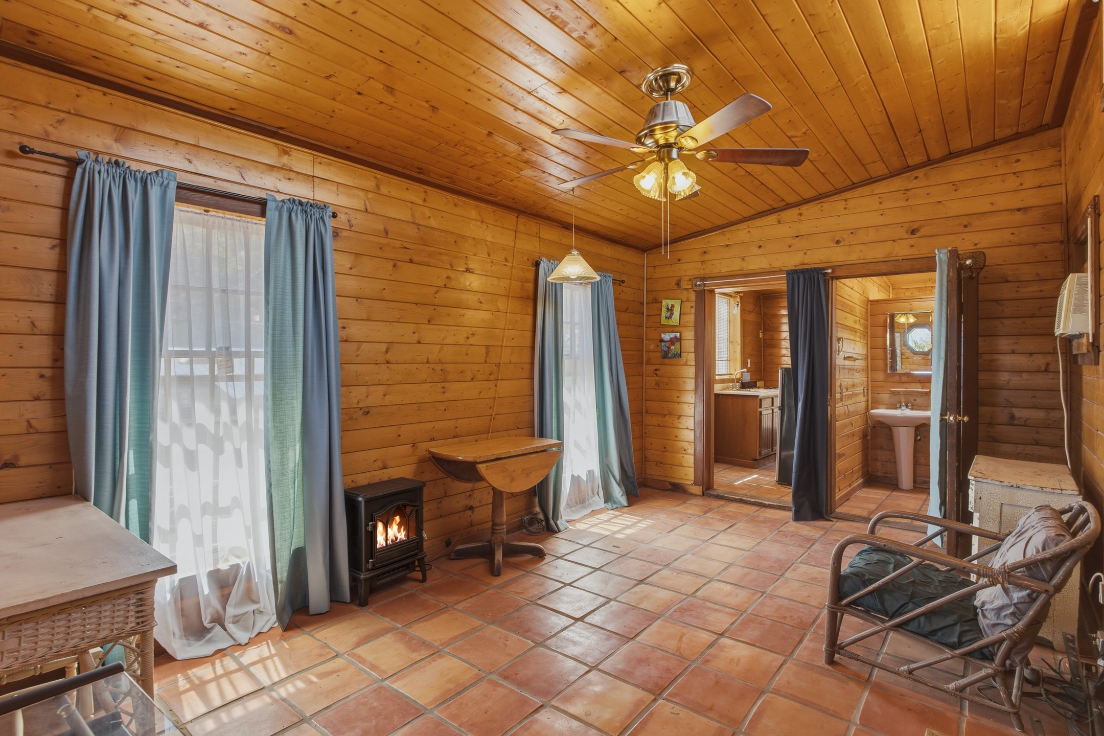 Wood-paneled cabin room with terracotta tile, a wood stove, and an open doorway to the bathroom.