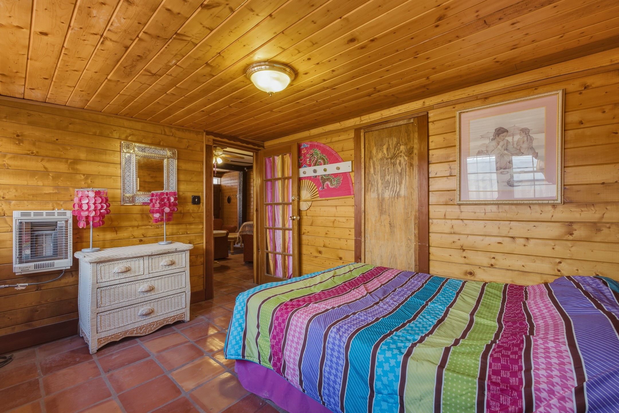 Bedroom with wood-paneled walls, a colorful striped bedspread, and terracotta tile flooring.
