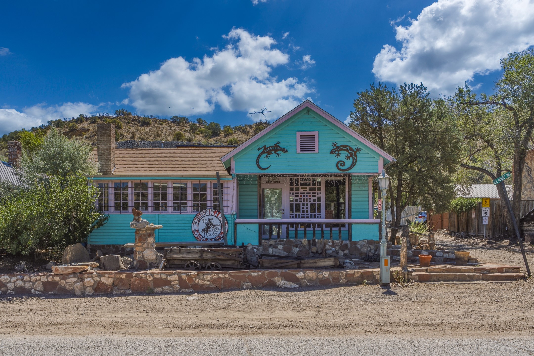 Turquoise building with pink trim, gecko decorations on its gable, and a stone-fronted porch.