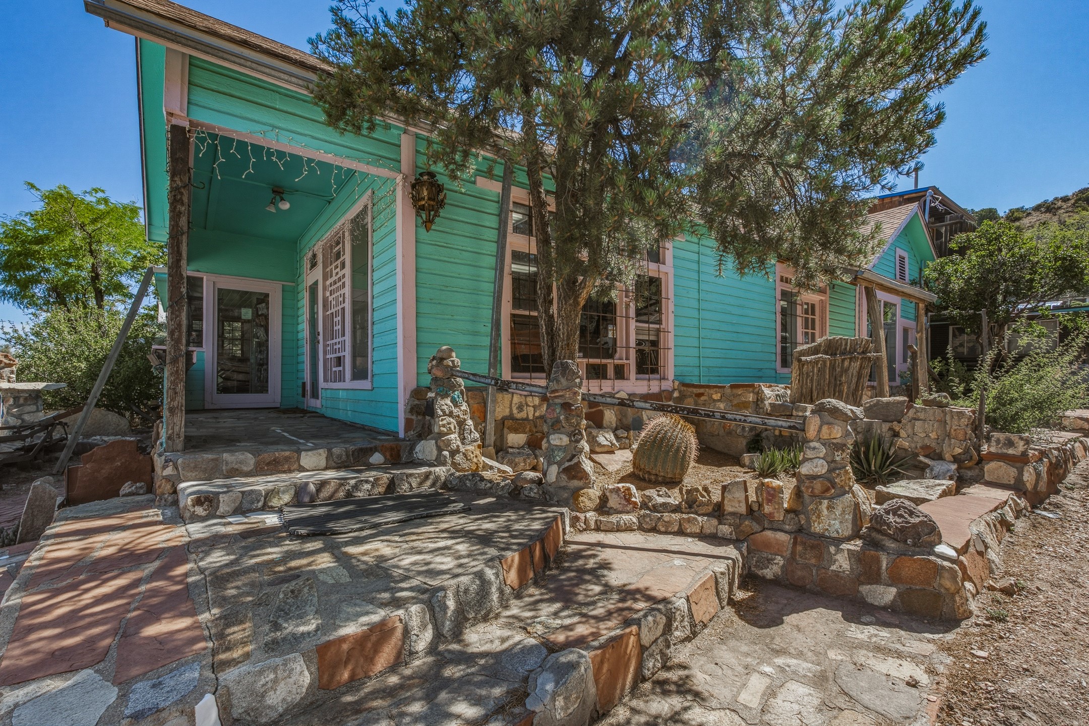 Turquoise house with pink trim behind a tiered stone patio and desert landscaping.