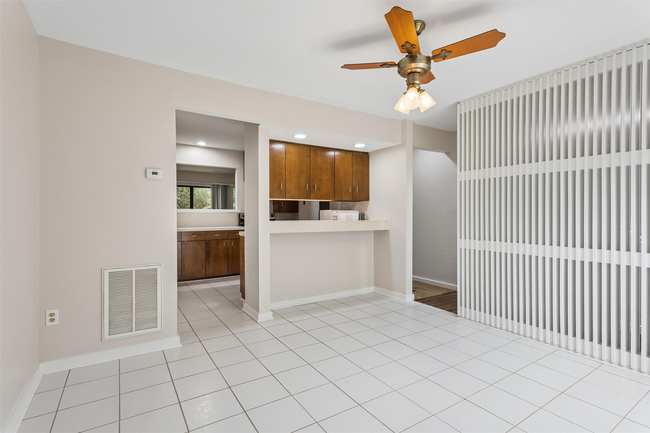 Empty tiled dining area with a ceiling fan, vertical blinds, and a kitchen breakfast counter.