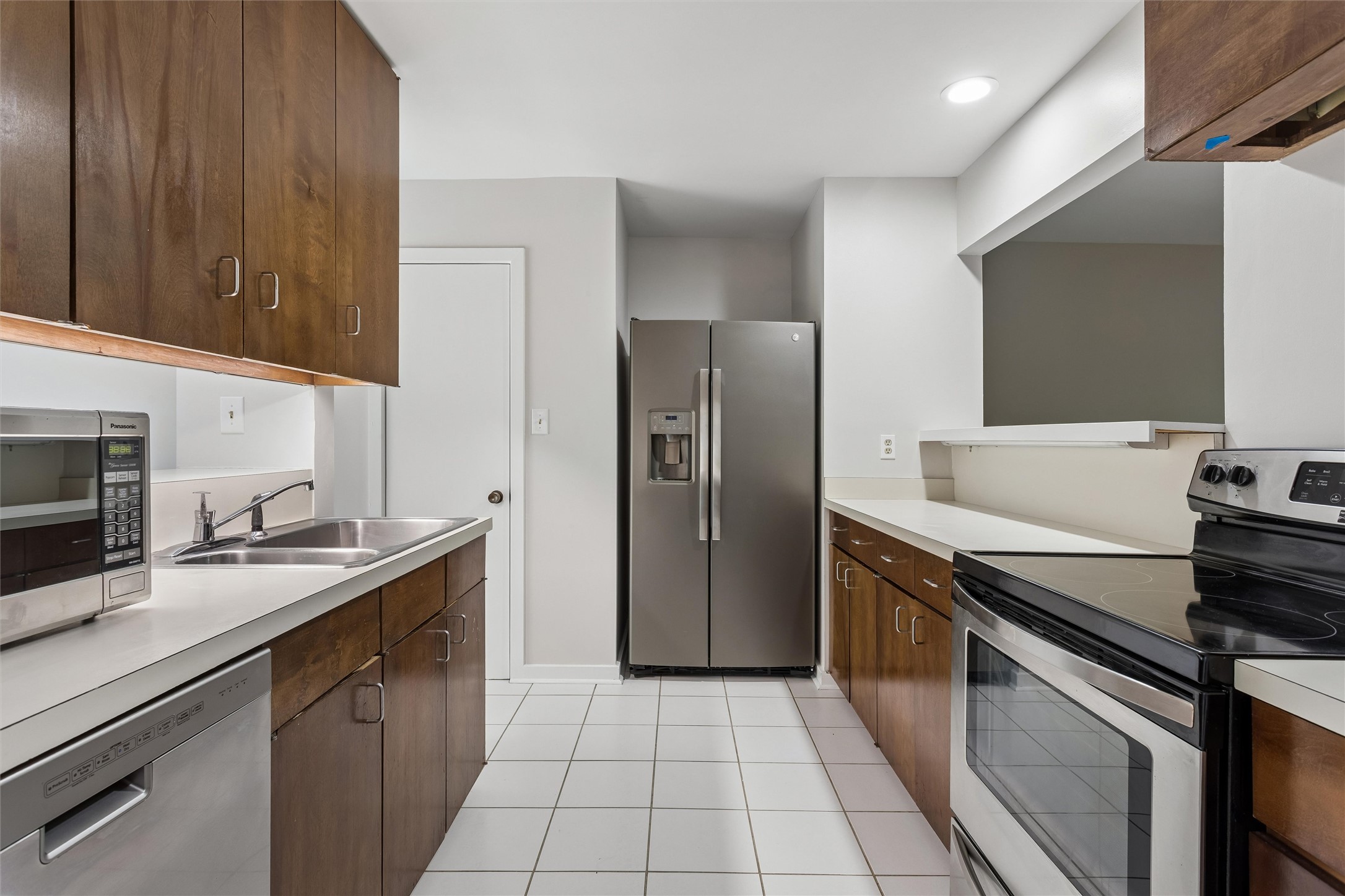 Kitchen with dark wood cabinets, white counters, and stainless steel appliances.