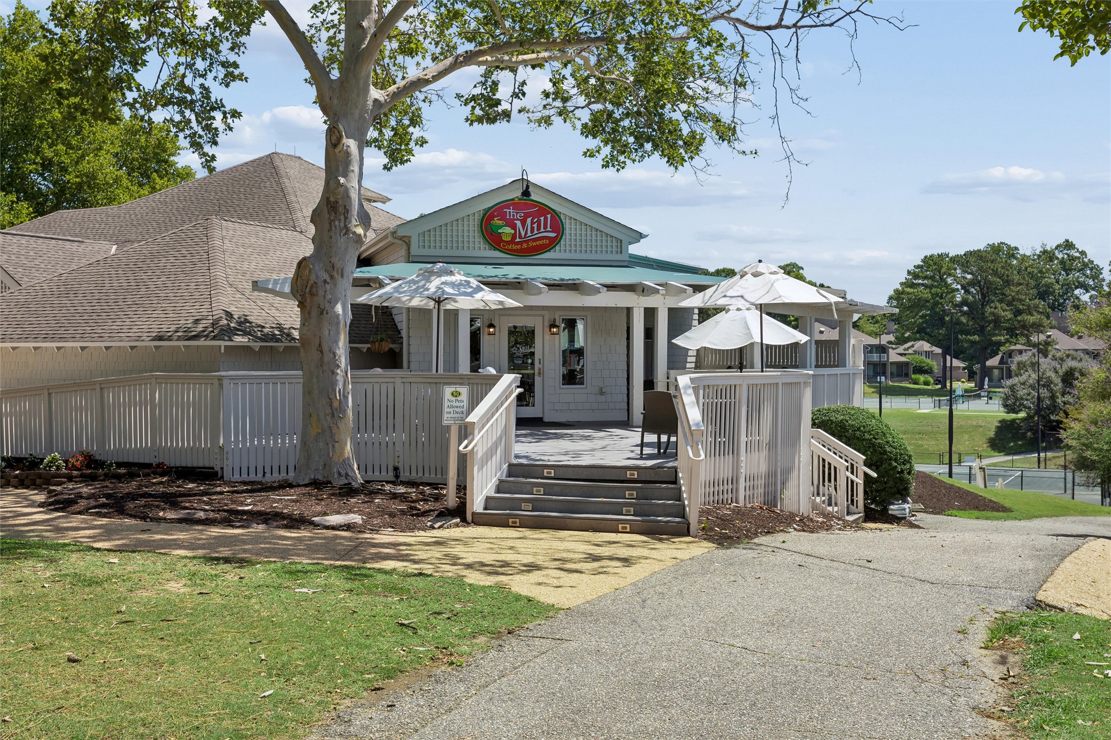 Café exterior with a white-railed deck, outdoor umbrellas, and a large tree in front.