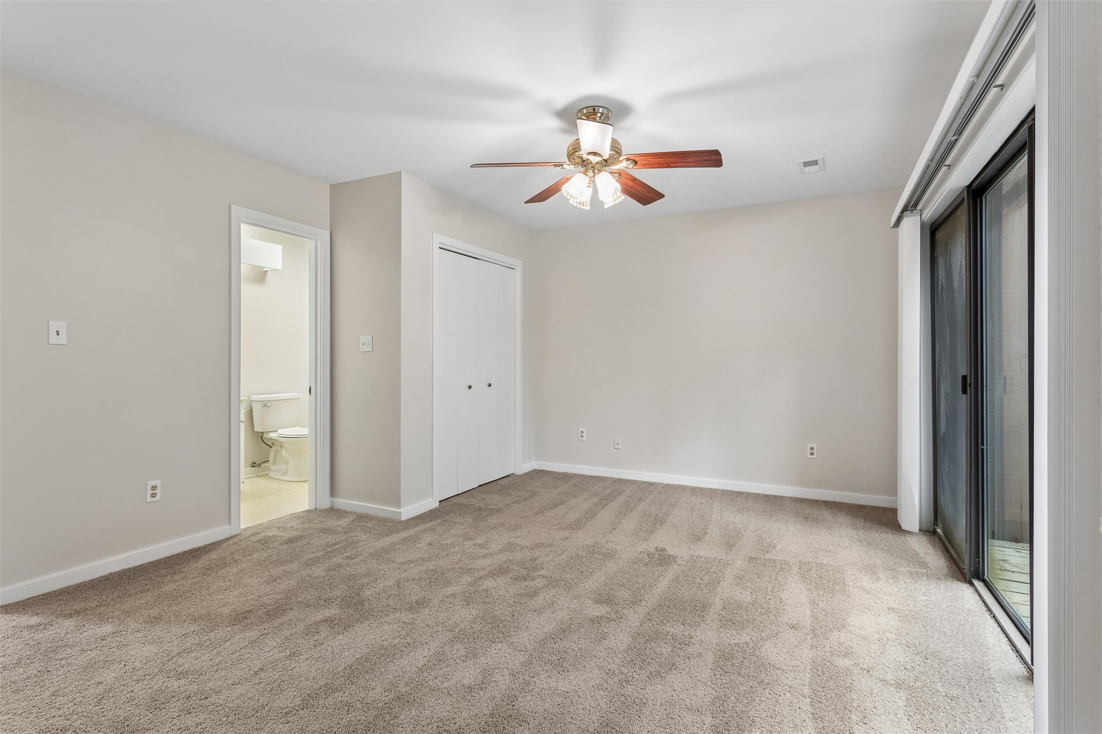 Empty carpeted bedroom with a ceiling fan, closet, and sliding glass doors to a deck.