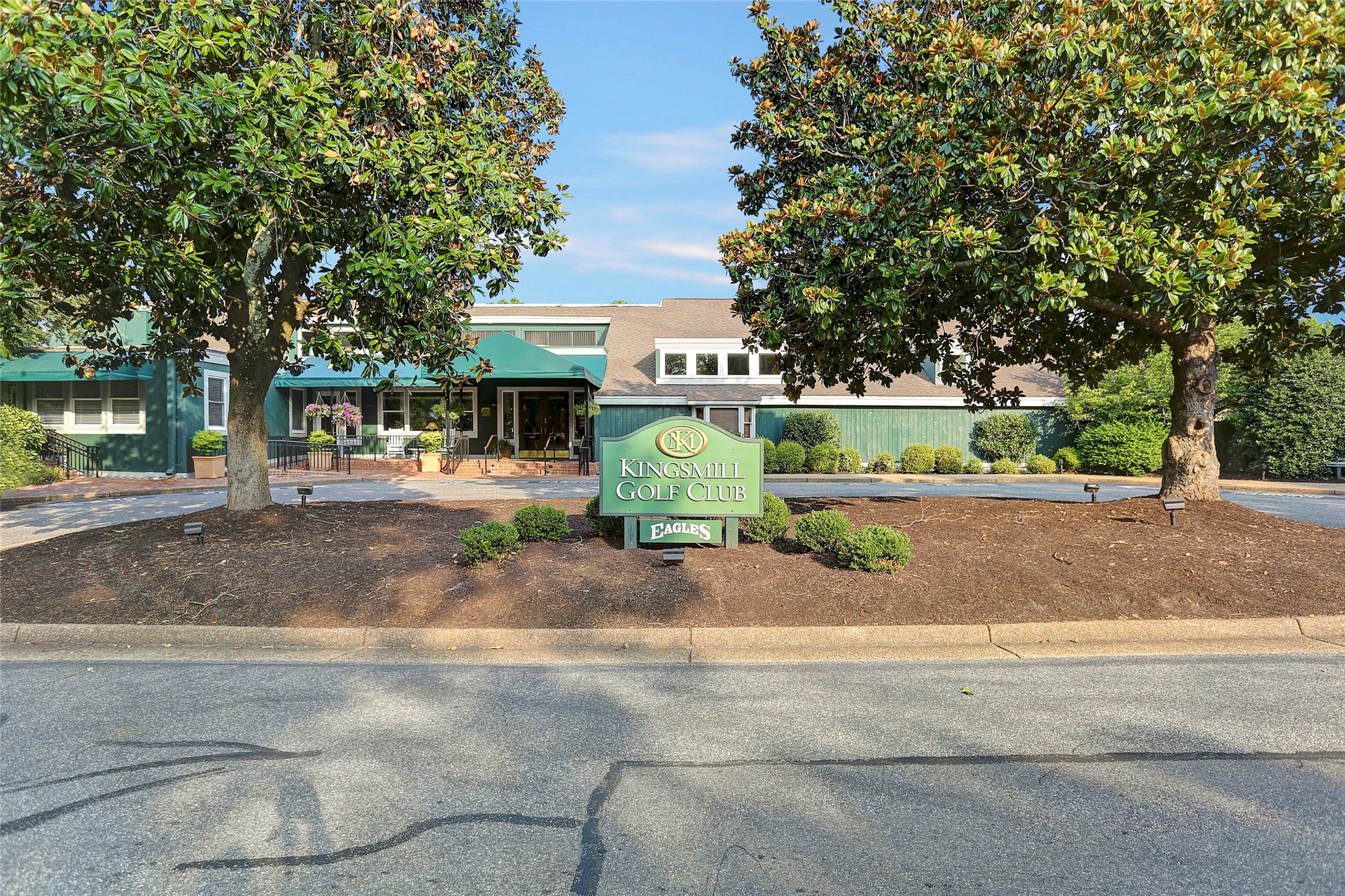 Kingsmill Golf Club exterior behind a green sign, framed by trees.