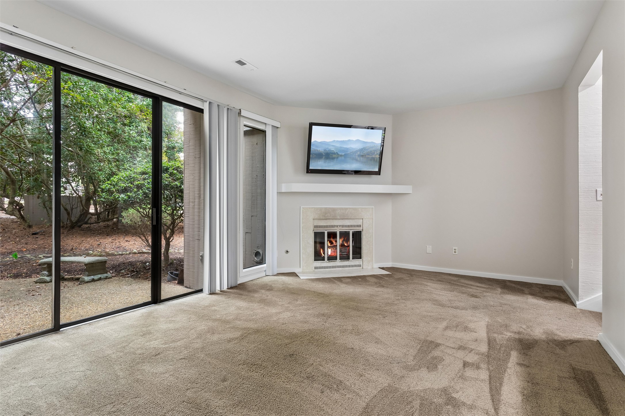Living room with a lit fireplace and sliding glass doors overlooking a leafy yard.