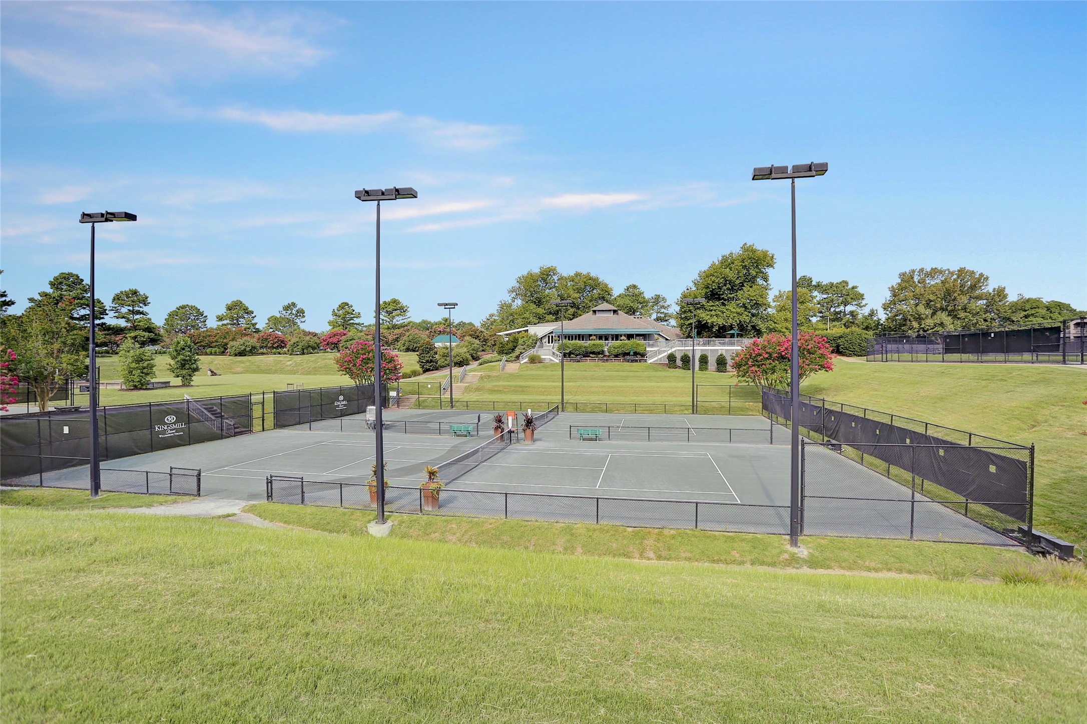 Community tennis courts with tall lights, landscaped grounds, and a clubhouse in the background.