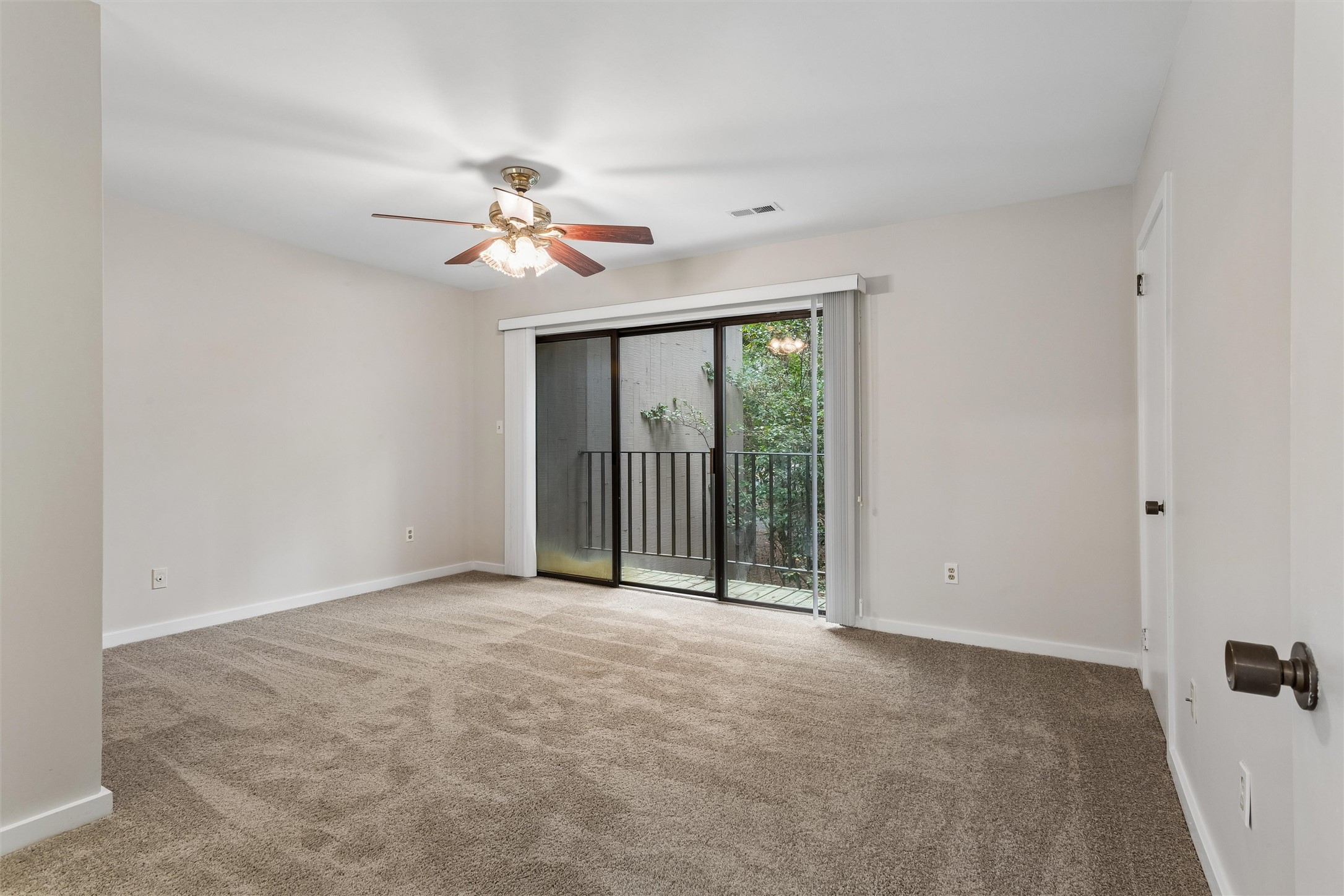 Empty carpeted room with a ceiling fan and sliding glass doors opening to a balcony.