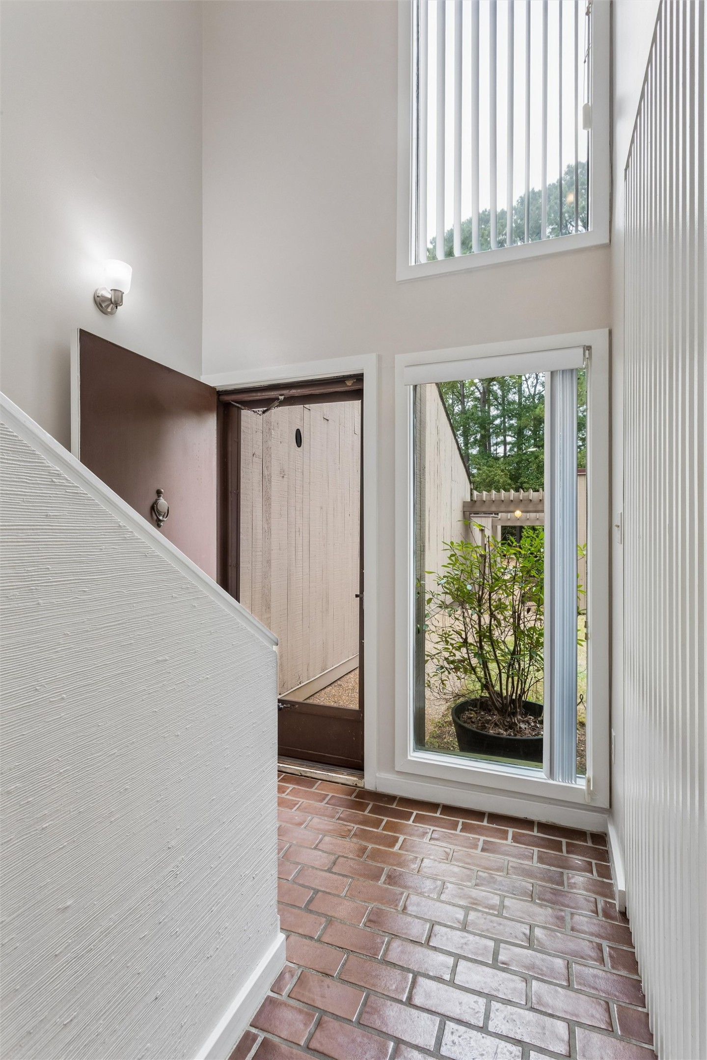 Entryway with brick-tile flooring, an open door, and tall windows overlooking a potted shrub.
