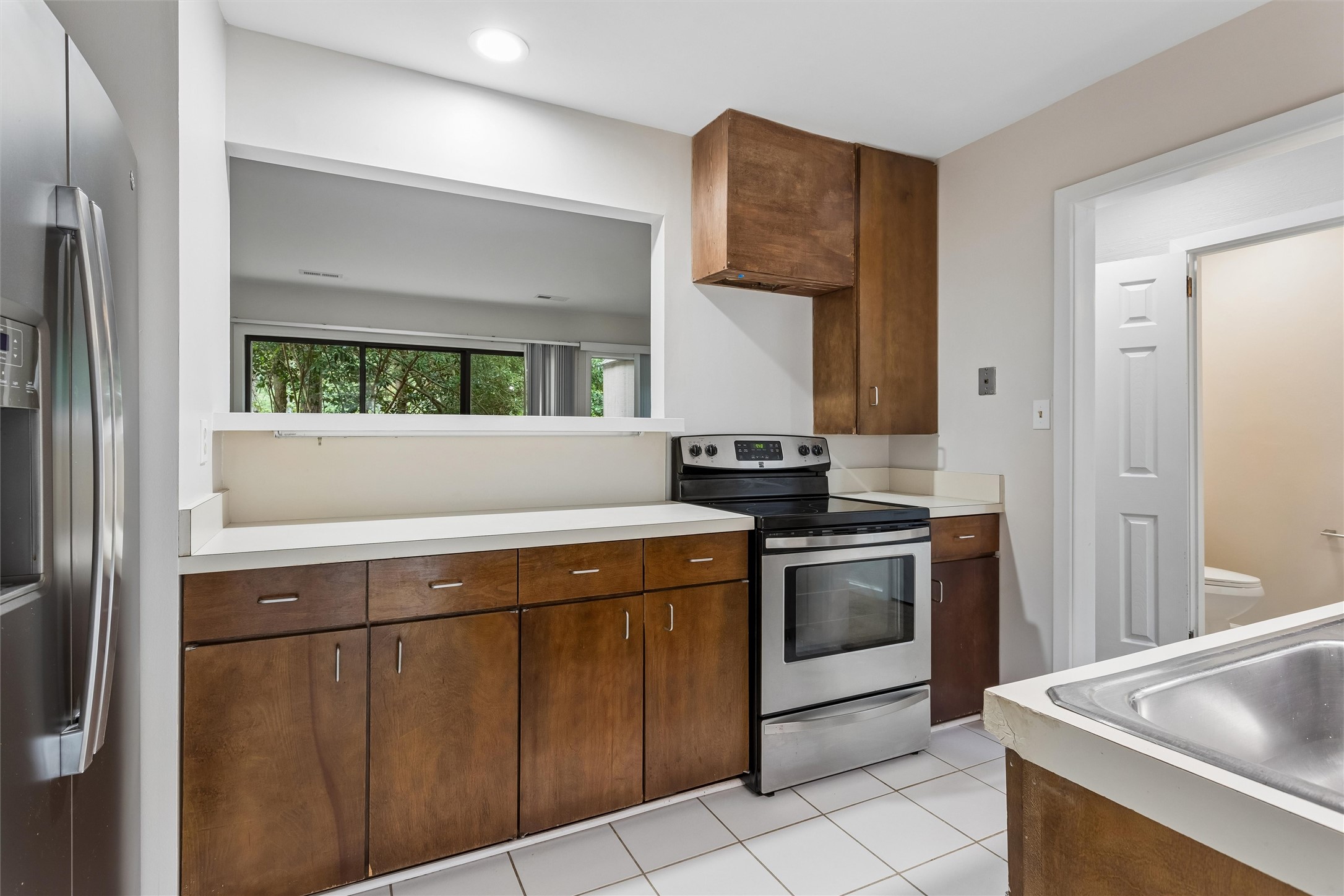 Kitchen with dark wood cabinets, stainless steel appliances, a pass-through, and a tiled floor.