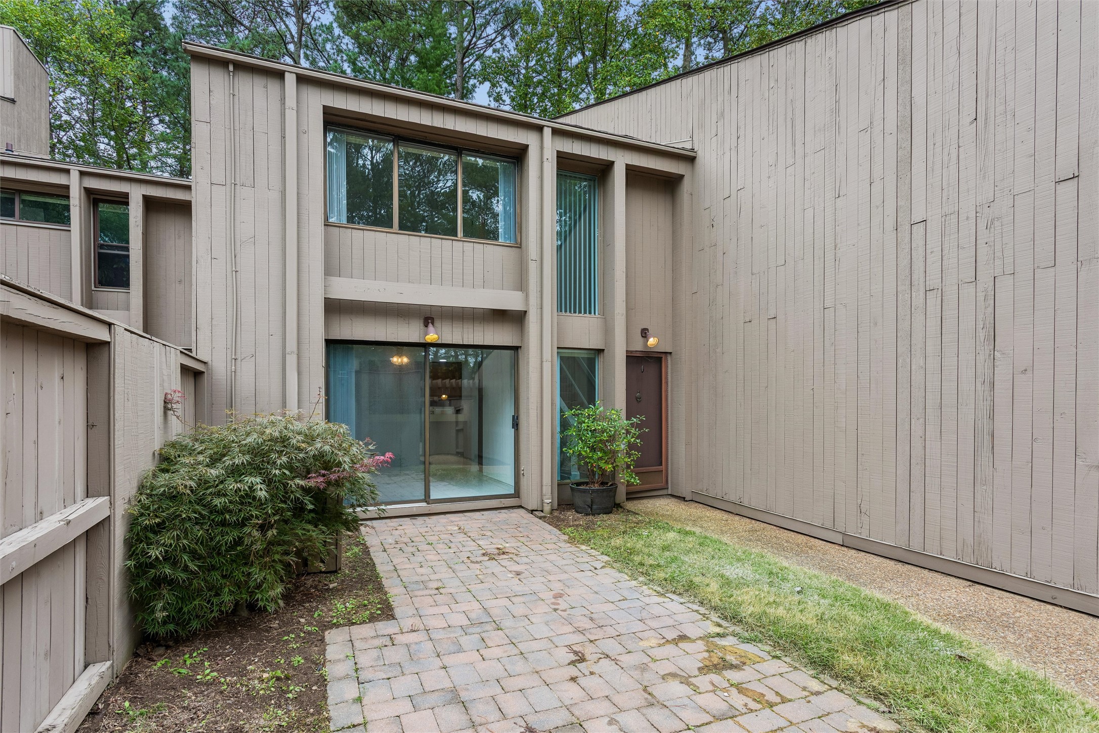 Two-story home with beige siding, large windows, and a brick-paved courtyard.