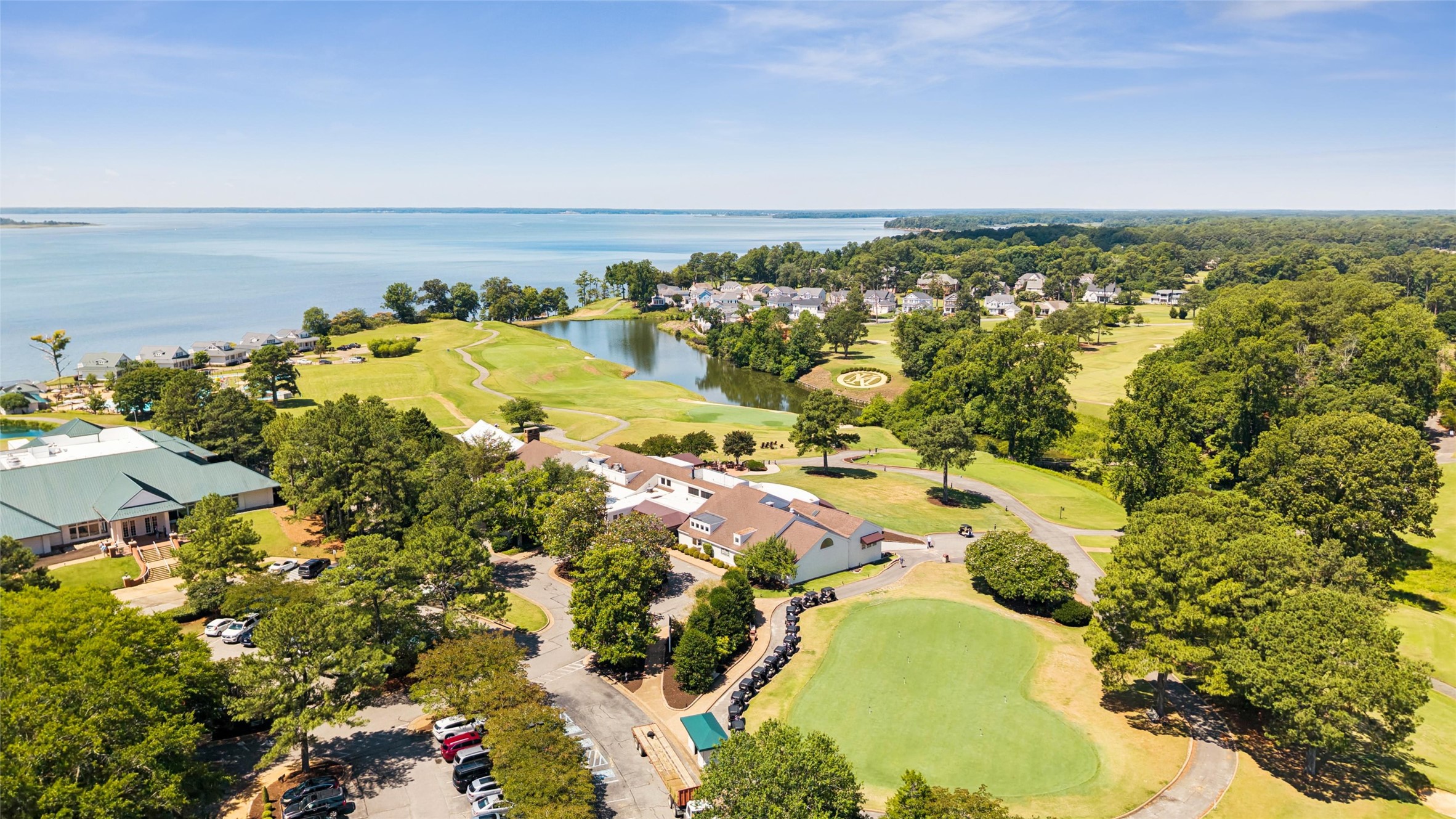 Aerial view of a waterfront golf course community with homes, clubhouse, and putting greens.