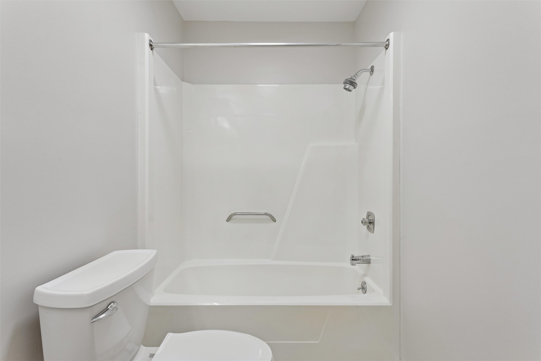 Bathroom with a white tub and shower, chrome fixtures, and part of a toilet.