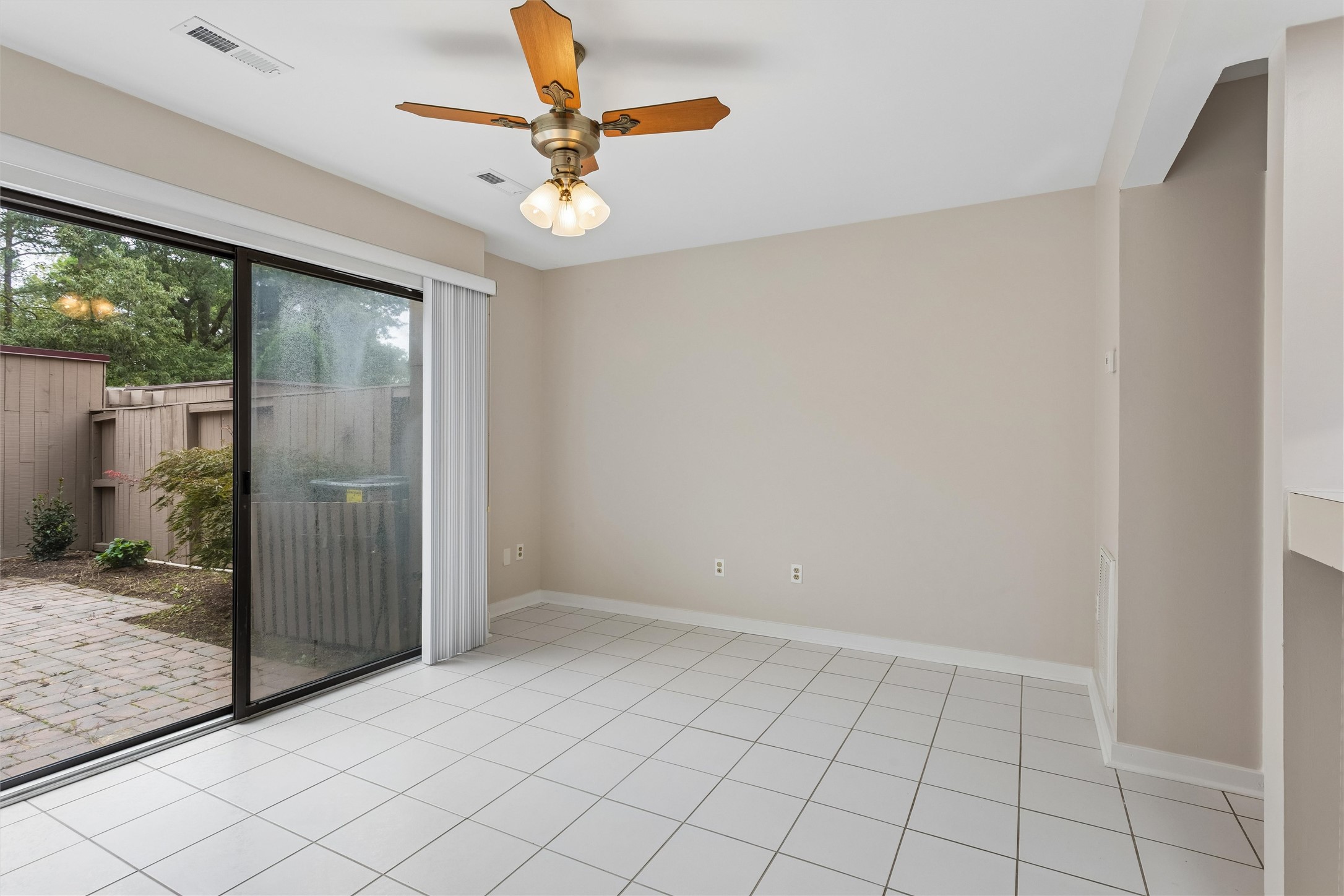 Empty tiled dining area with a ceiling fan and sliding glass door to a fenced patio.