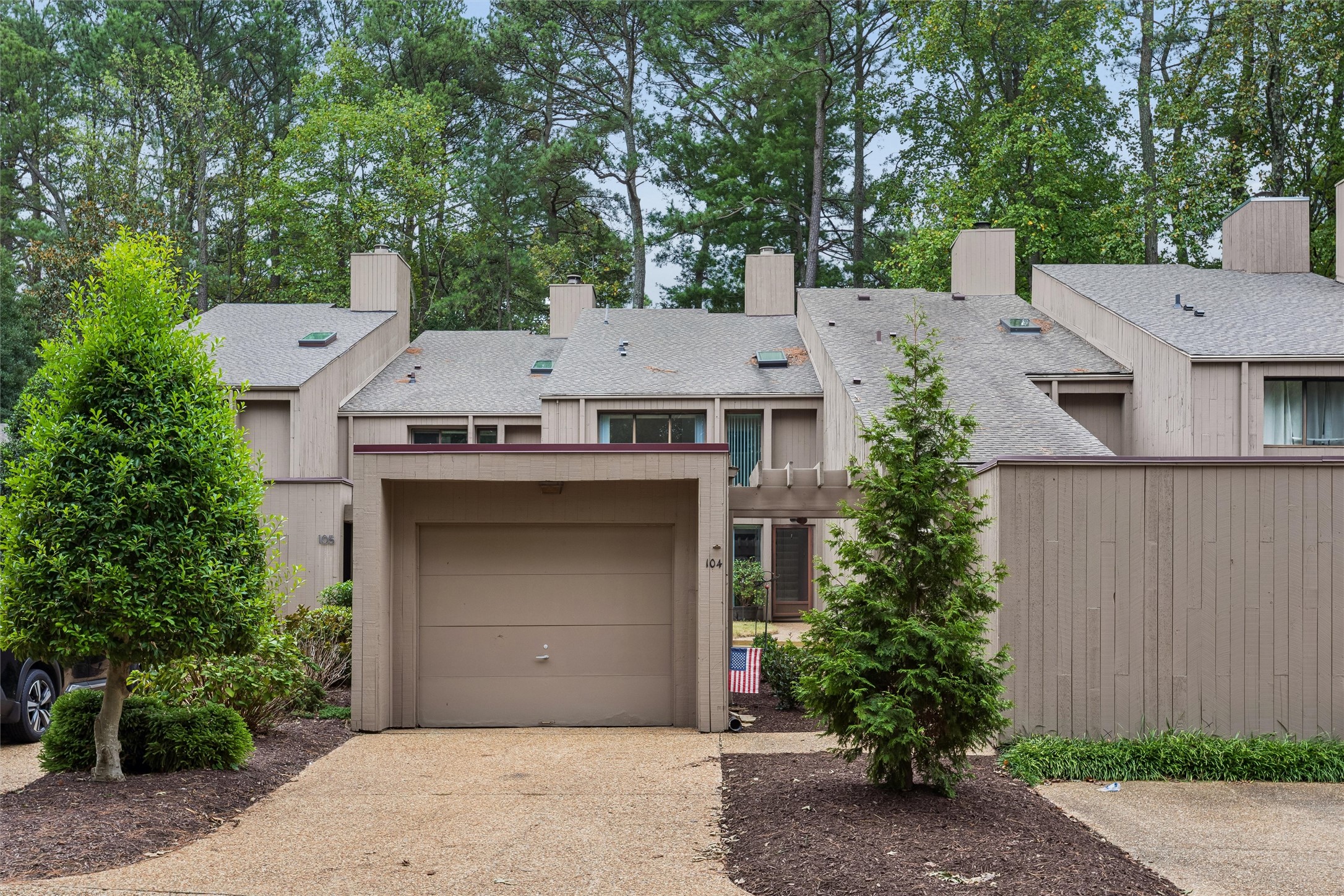 Attached townhouse with a garage, landscaped entrance, and American flag.