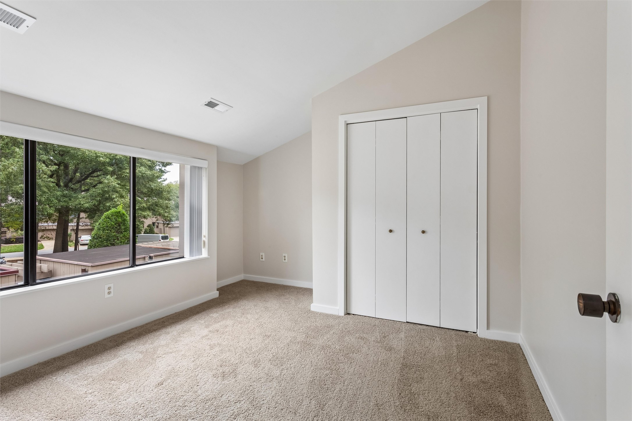 Vacant bedroom with a wide window overlooking trees and a large white folding-door closet.