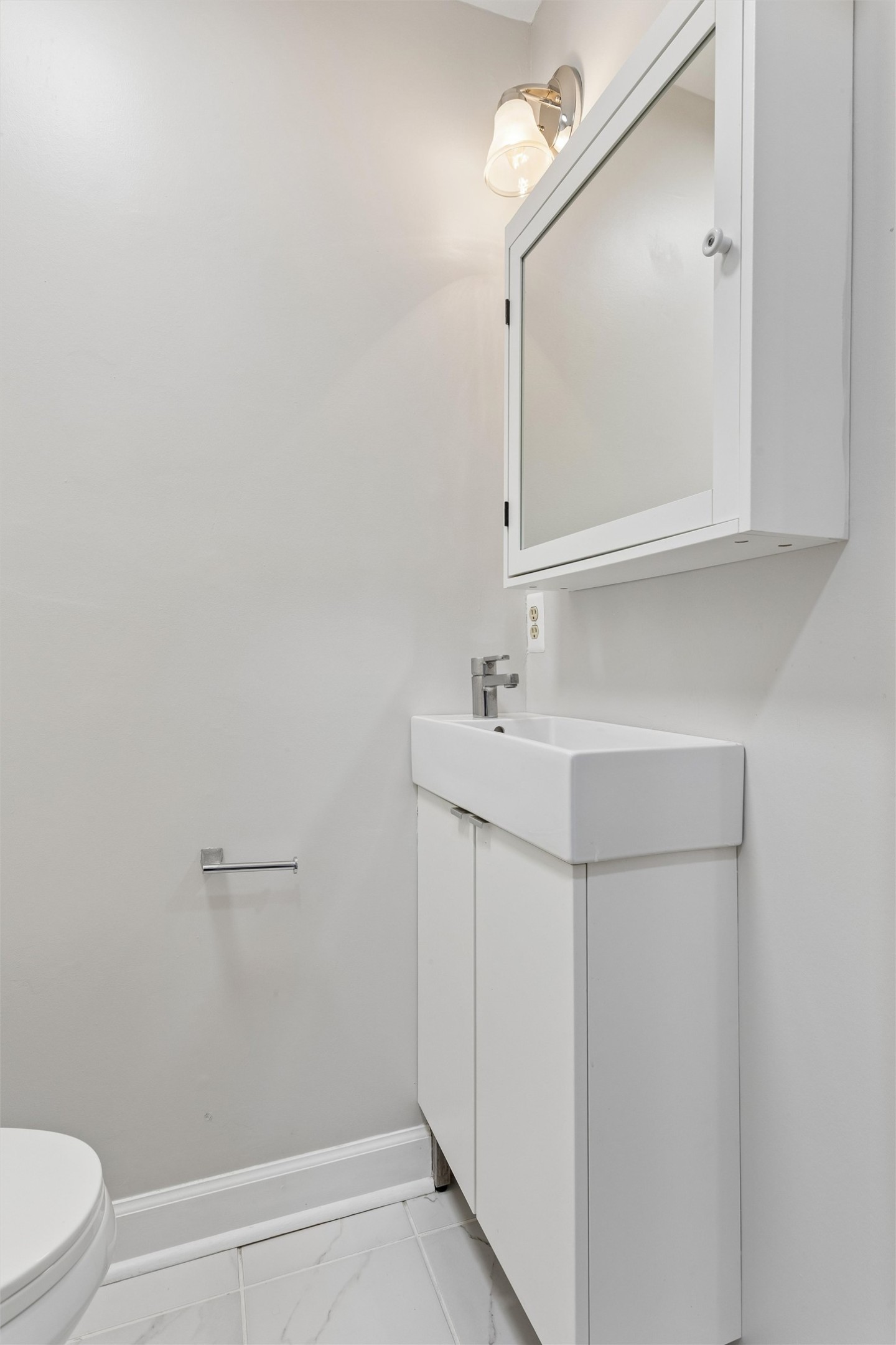Bathroom with a white rectangular sink, mirrored medicine cabinet, and partial view of the toilet.