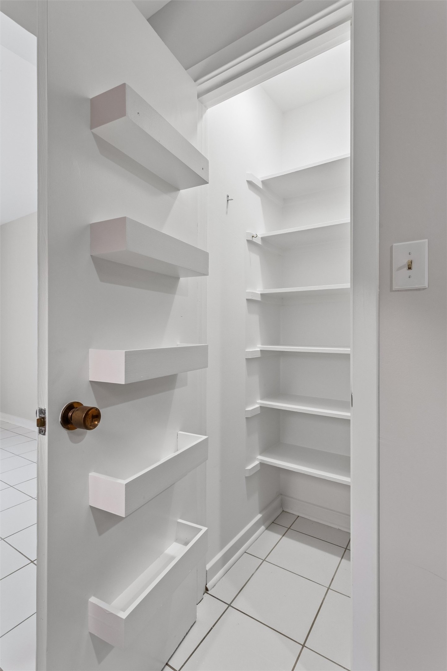 White walk-in pantry with built-in corner shelves and shelving on the open door.