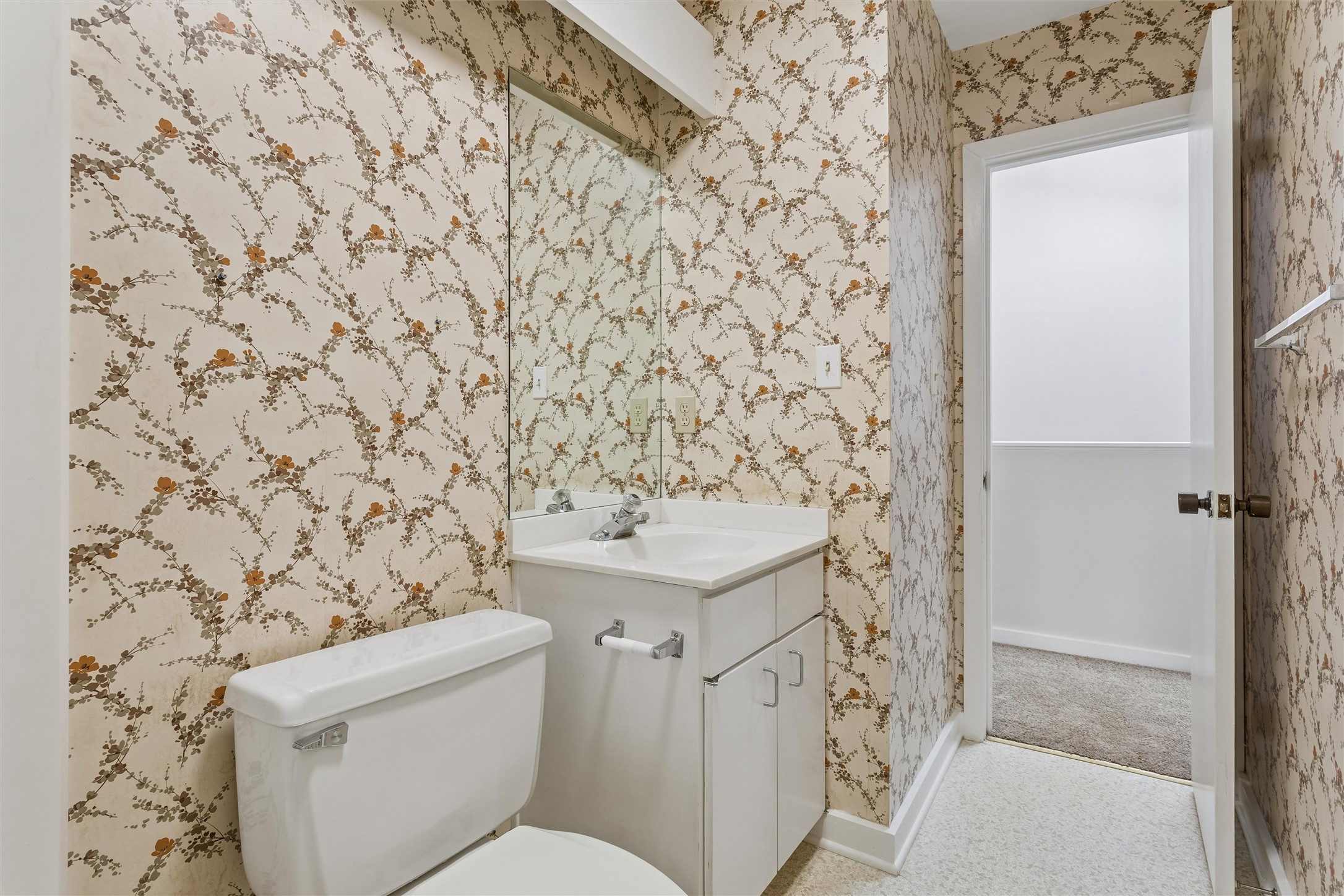 Bathroom with floral vine wallpaper, a white toilet, and a vanity with a large mirror.