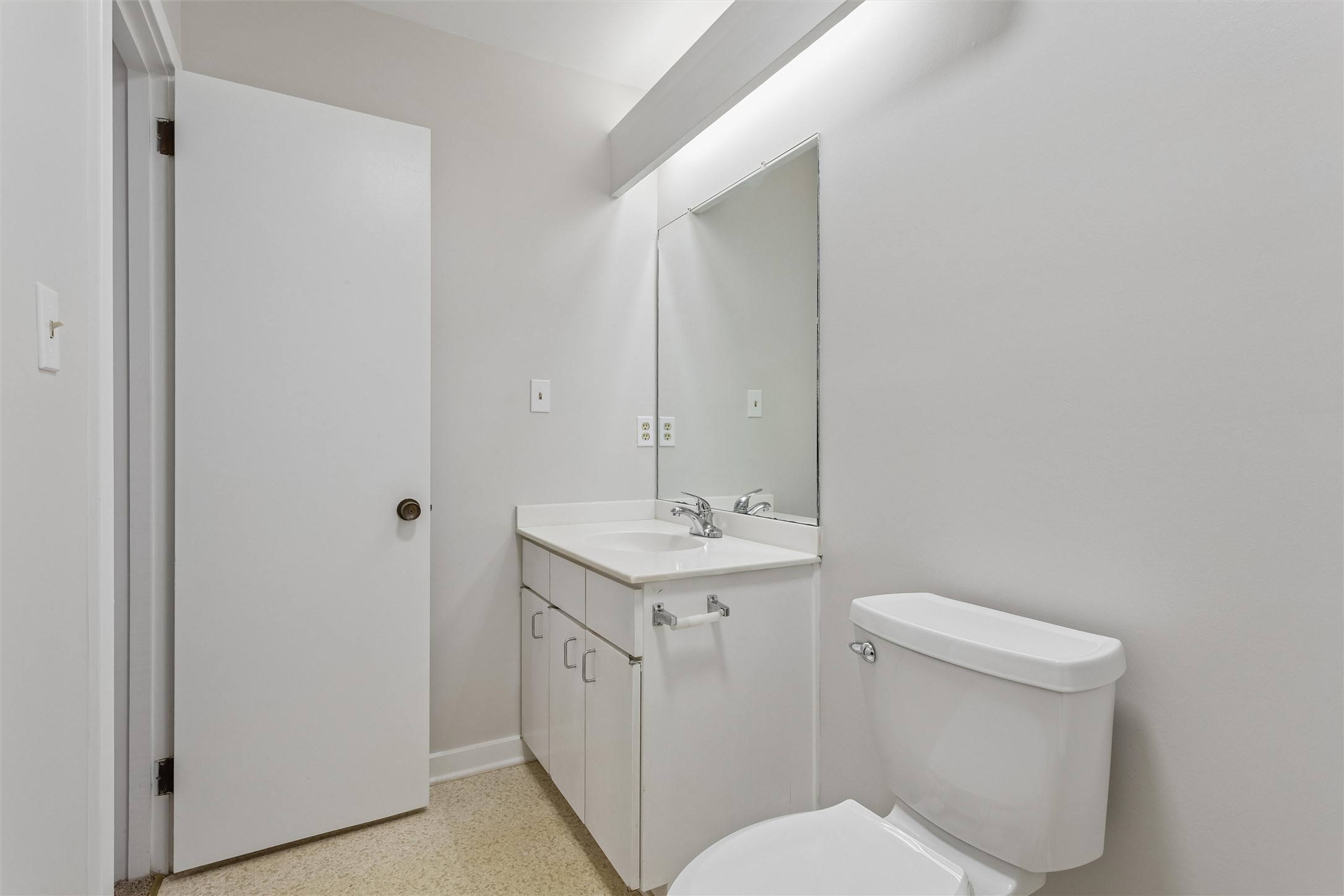 Bathroom with a white vanity, large mirror, and toilet beside an open door.