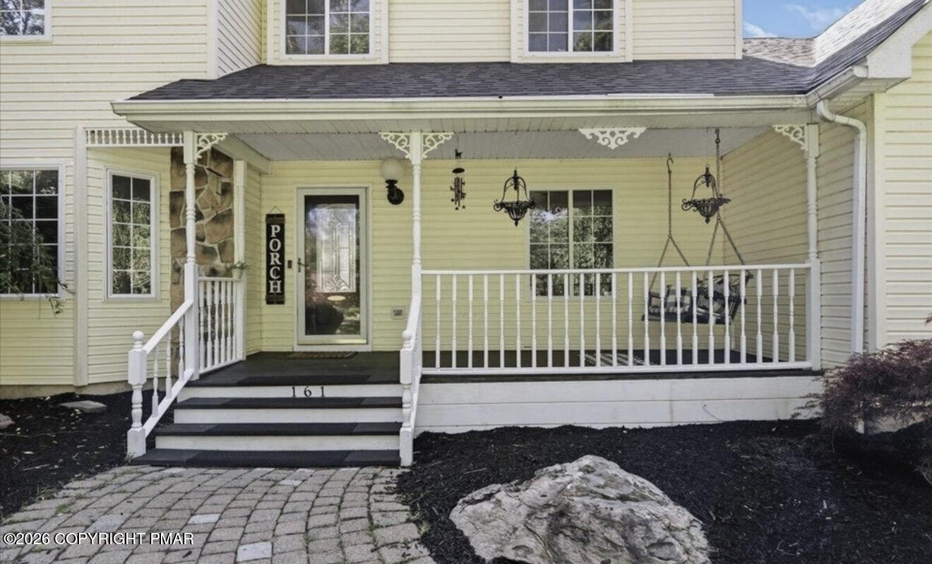 Pale yellow house with a covered front porch, white railings, and a hanging swing.