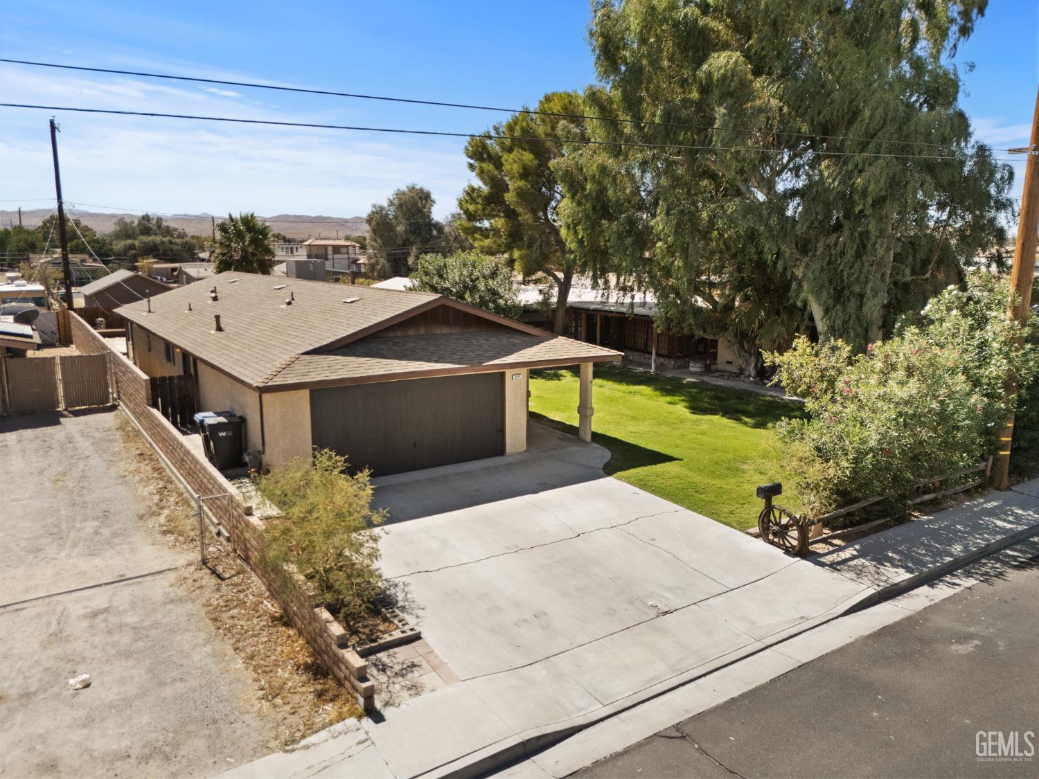 Aerial view of a single-story home with an attached garage, carport, wide driveway, and green front lawn.