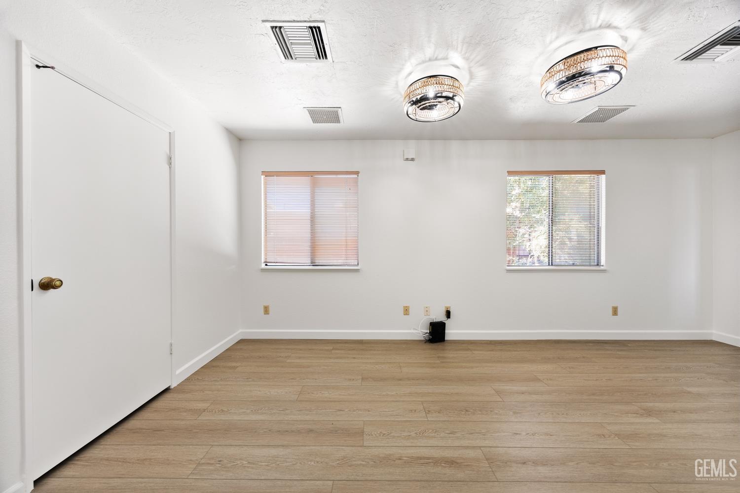 Vacant room with wood-look flooring, two blinded windows, and circular ceiling lights.
