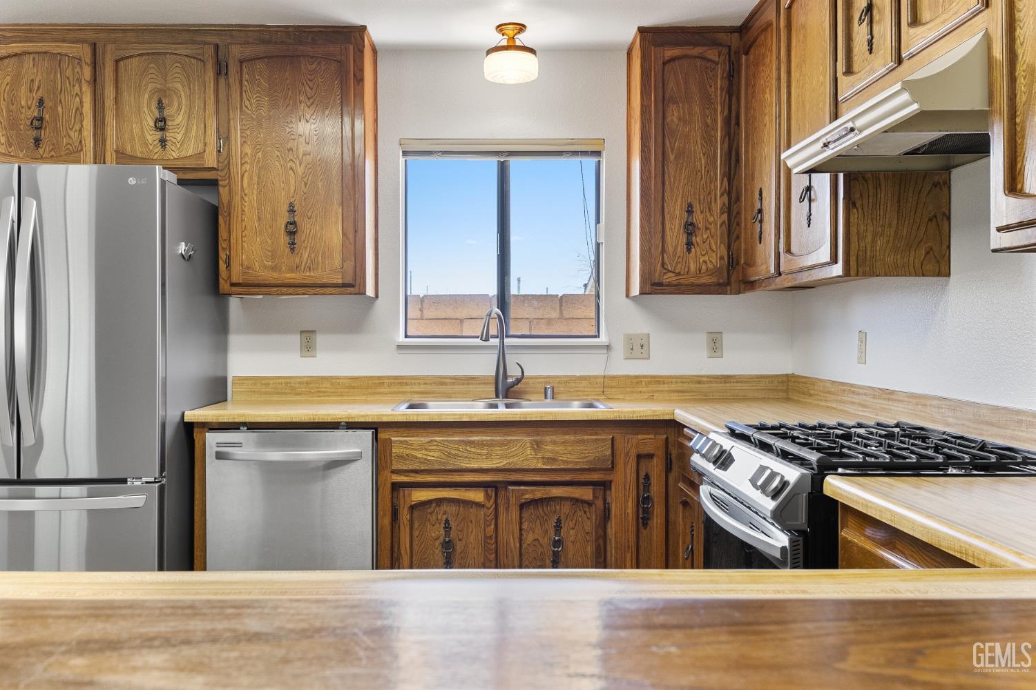 Kitchen with honey-colored wood cabinets, stainless appliances, and a gas range beside the sink window.