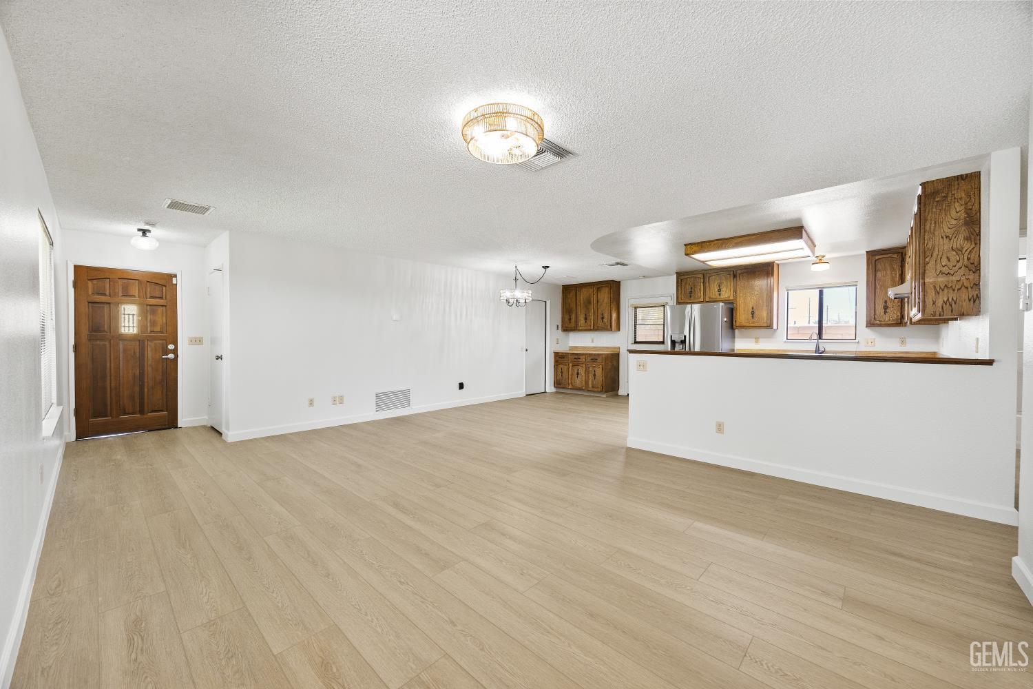 Unfurnished open-plan living and dining area with light flooring and a kitchen with dark wood cabinets.