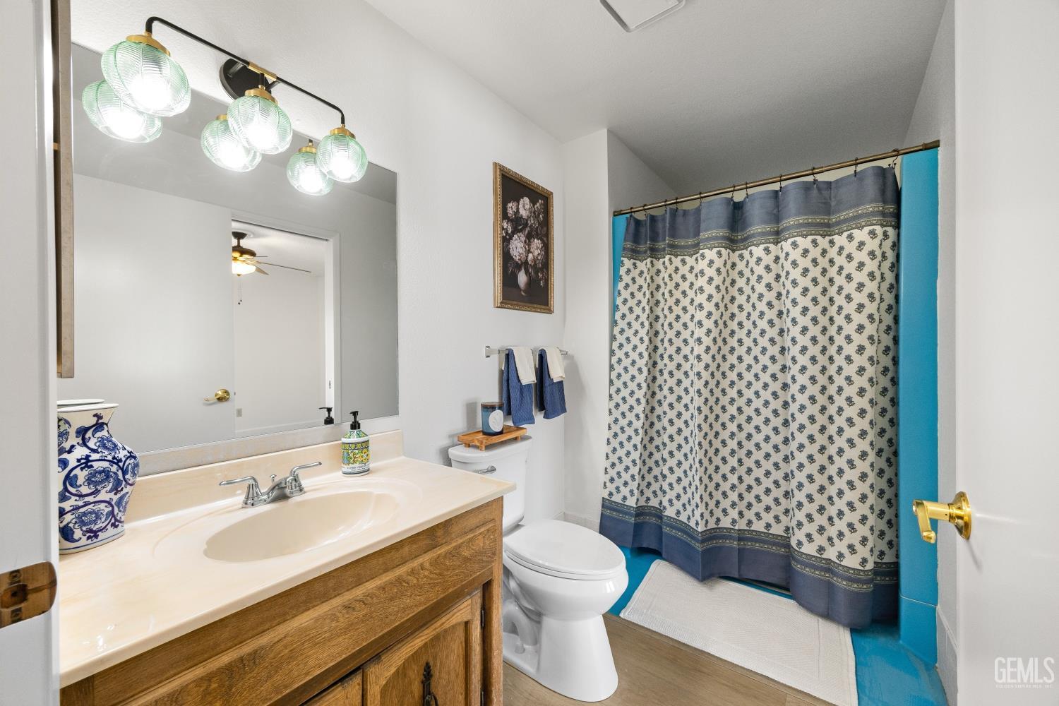 Bathroom with a wood vanity, large mirror, and patterned shower curtain framed by turquoise walls.