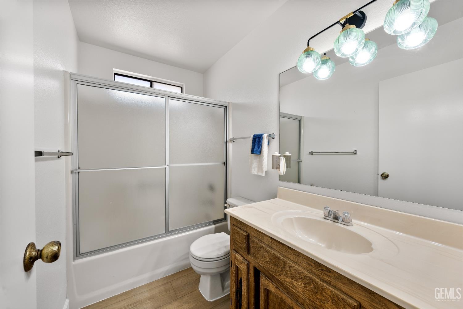 Bathroom with frosted sliding tub doors, a wood vanity, and a large mirror.