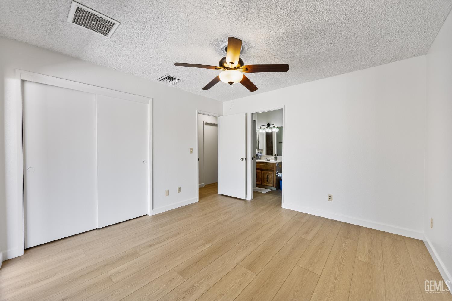 Empty bedroom with wood-look flooring, ceiling fan, and sliding closet doors.