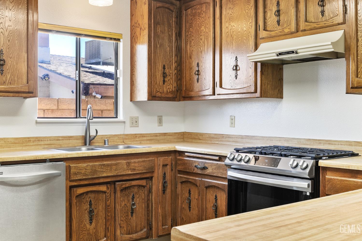 Kitchen with wood cabinets, butcher-block counters, stainless gas range, and a double sink beneath a window.