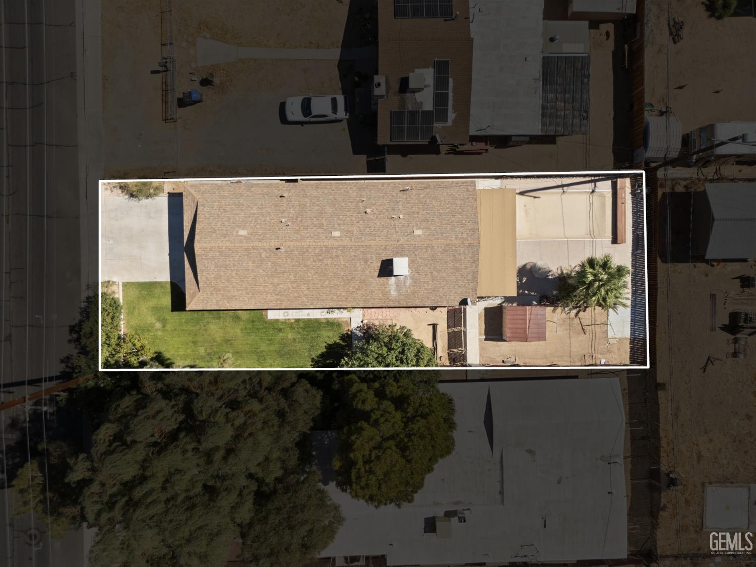 Aerial view of the outlined property, with a long shingle roof, green lawn, and palm trees.
