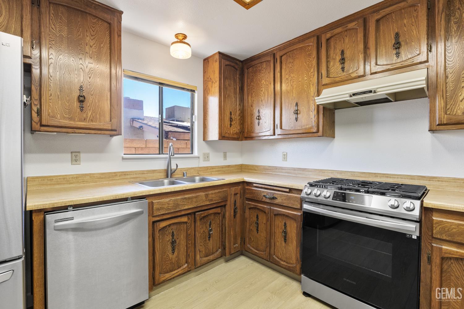 Kitchen with honey-toned wood cabinets, a double-basin sink, and a stainless-and-black gas range.
