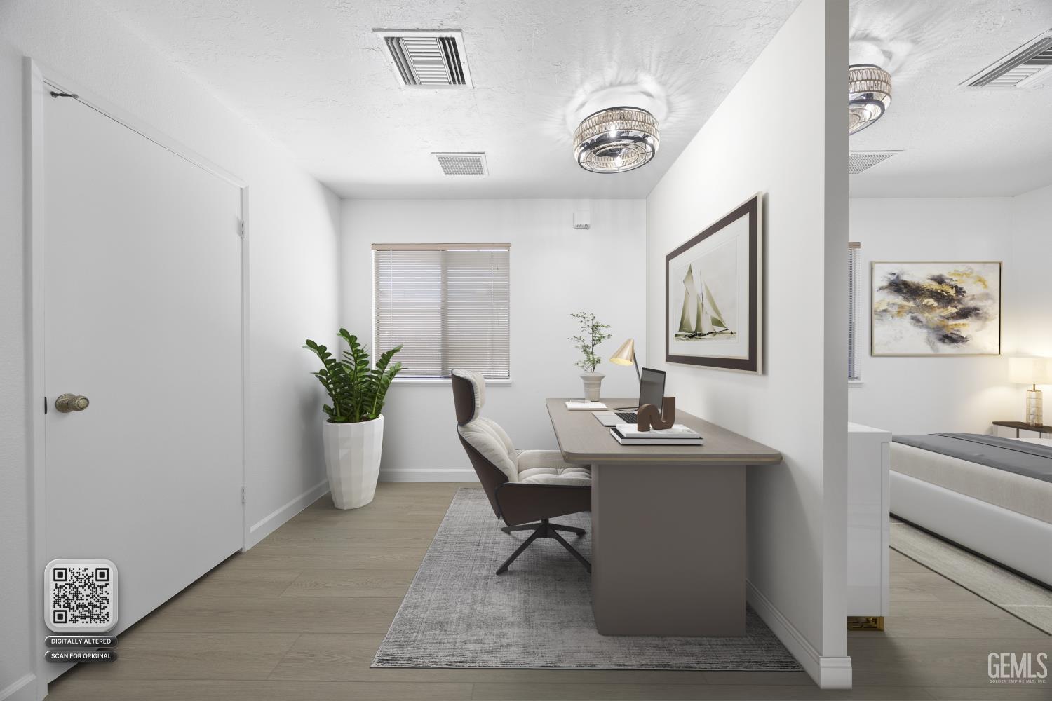 Home office with a gray desk and chair, potted plant, and view into an adjoining bedroom.