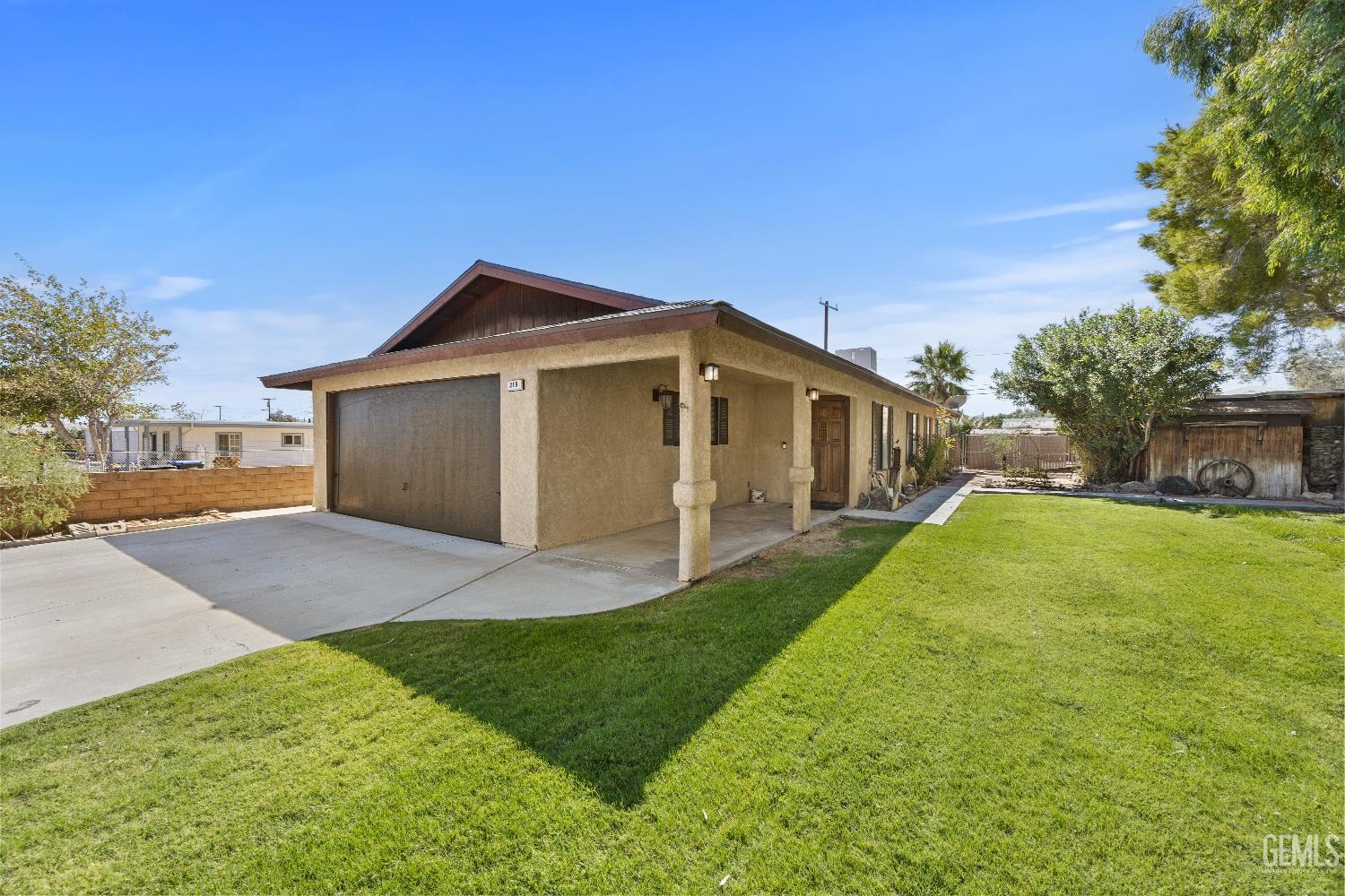 Single-story stucco house with a covered porch, double garage, and broad green lawn.