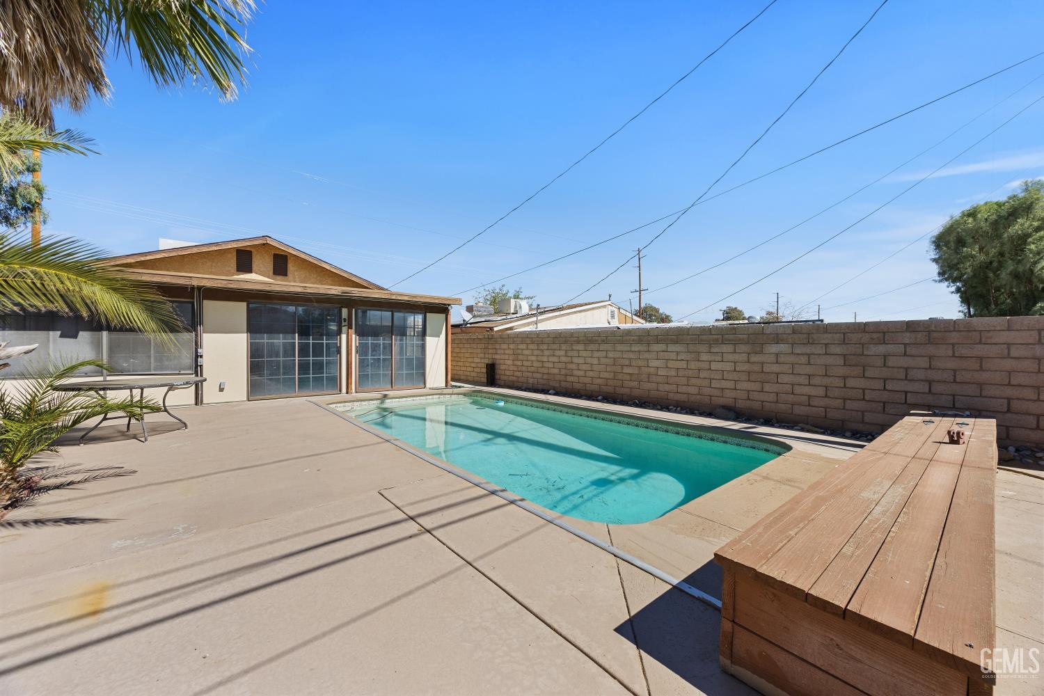 Backyard swimming pool beside a broad patio and long wooden bench.