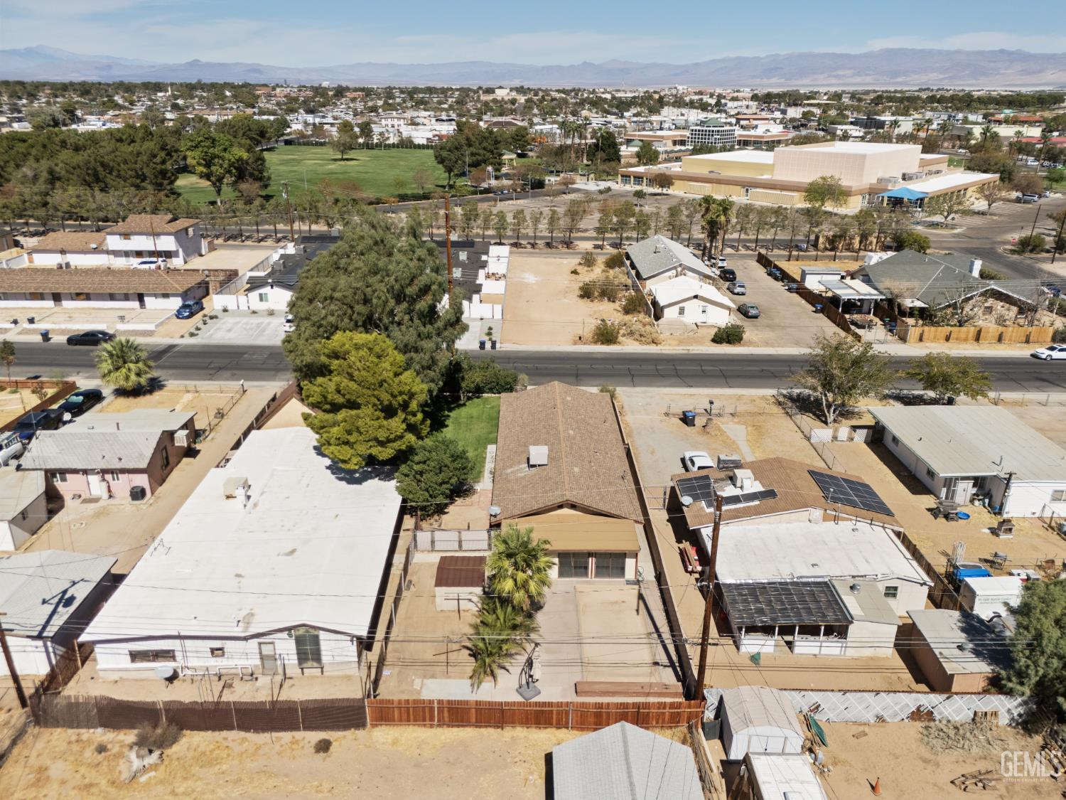 Aerial view of a fenced home and neighboring properties, with mountains in the distance.