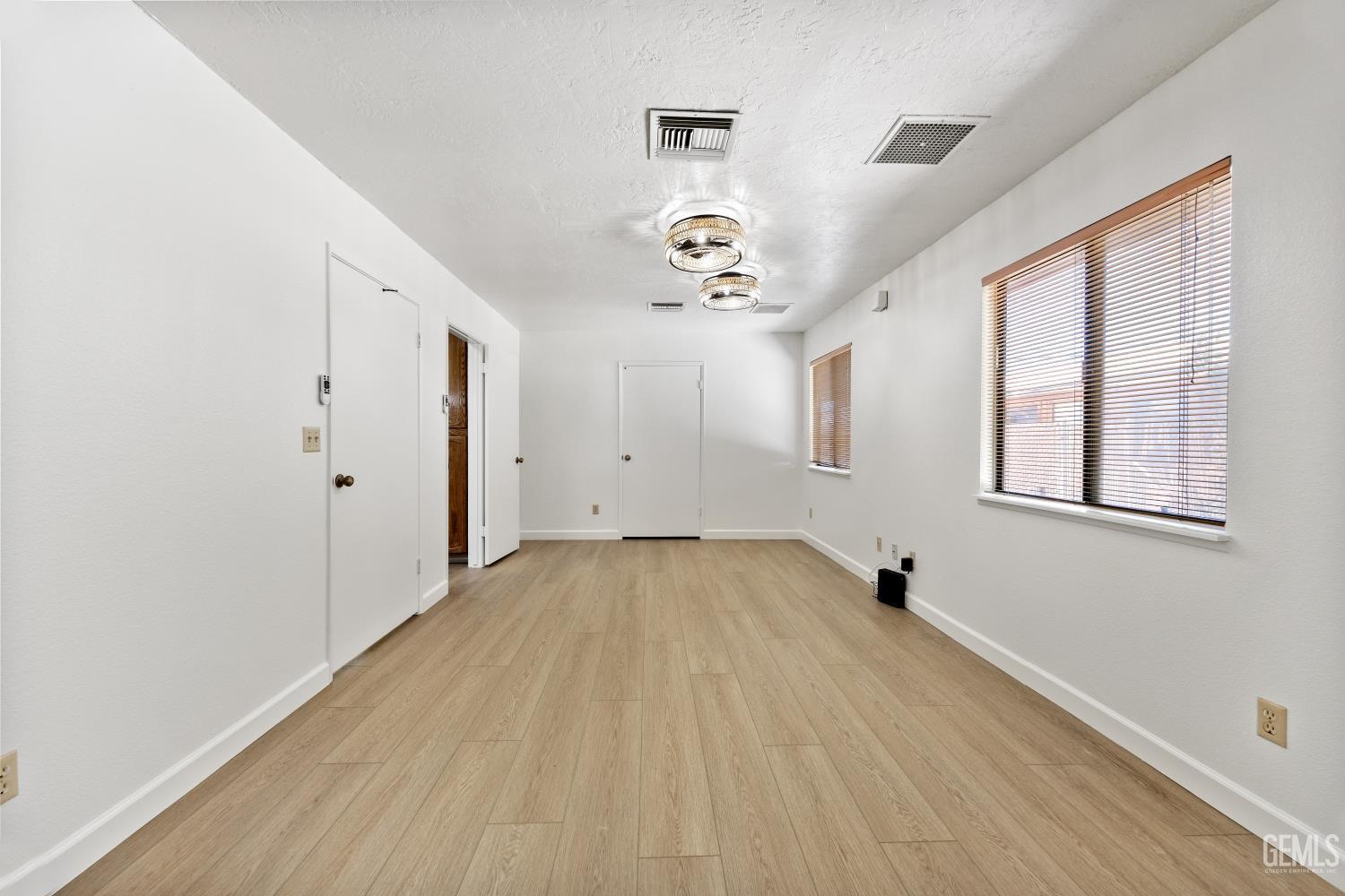Vacant narrow room with light wood-look flooring, window blinds, and two ceiling lights.