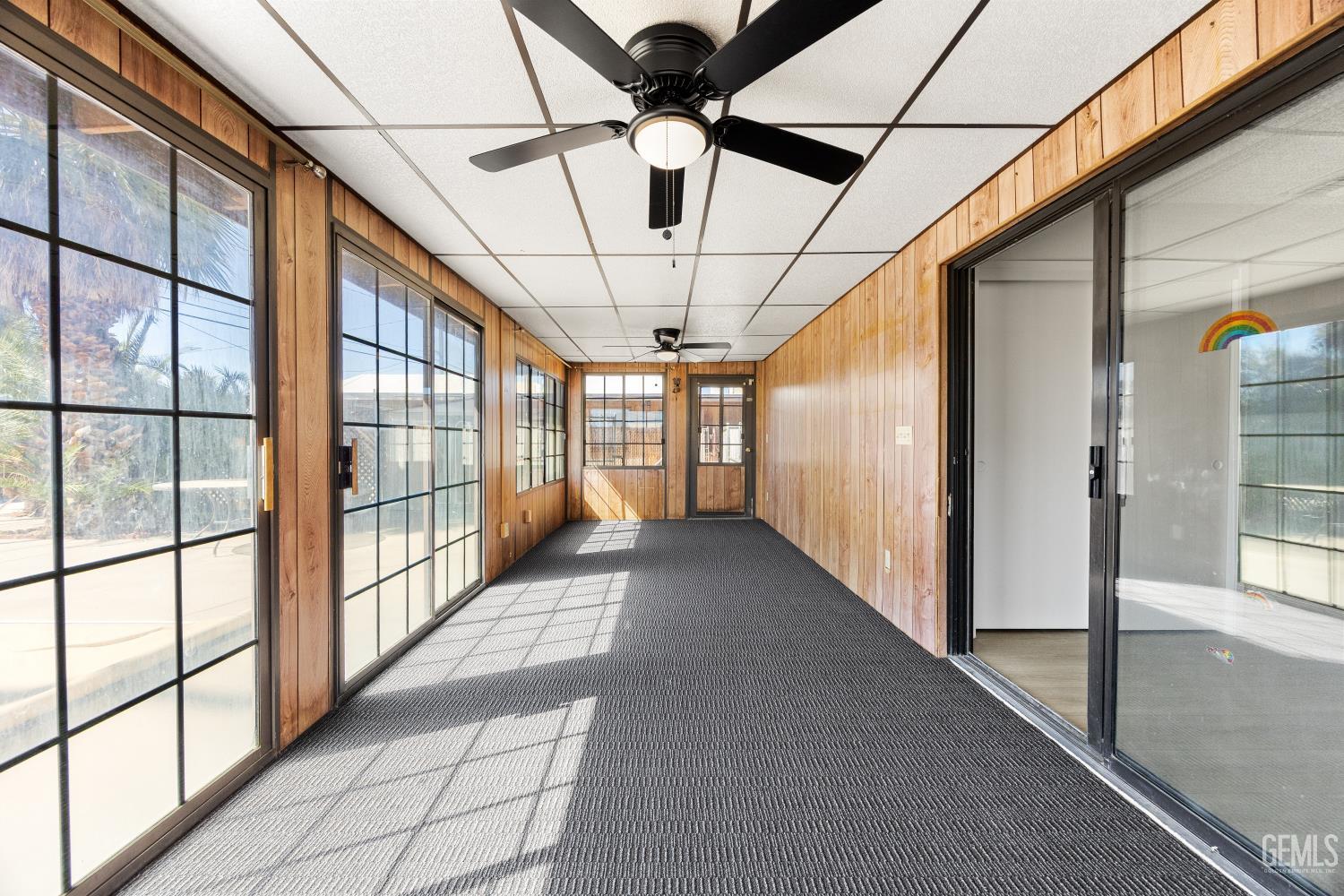 Enclosed sunroom with wood-paneled walls, black-framed windows, dark carpet, and ceiling fans.