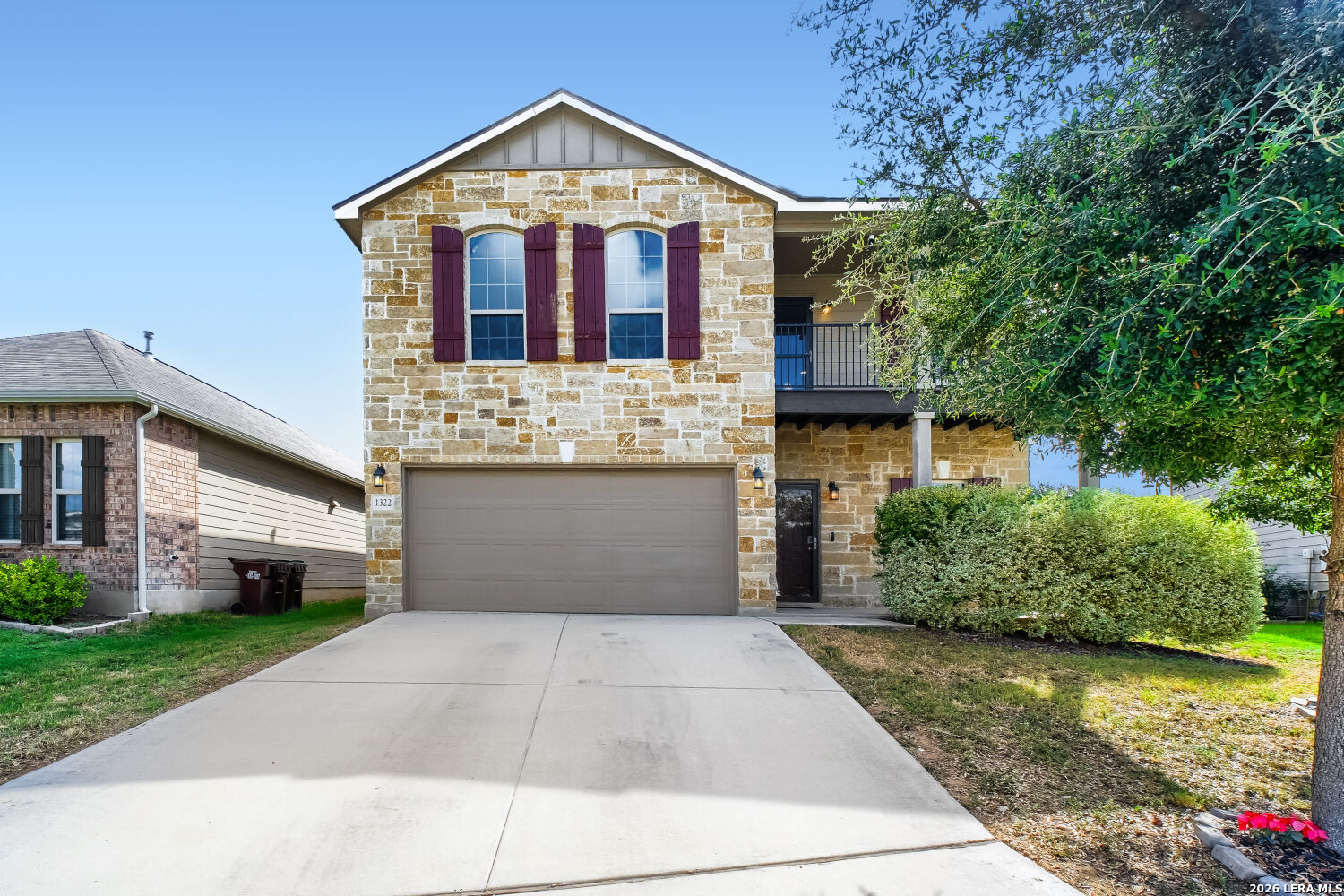 Two-story stone house with burgundy shutters, a two-car garage, and an upper balcony.