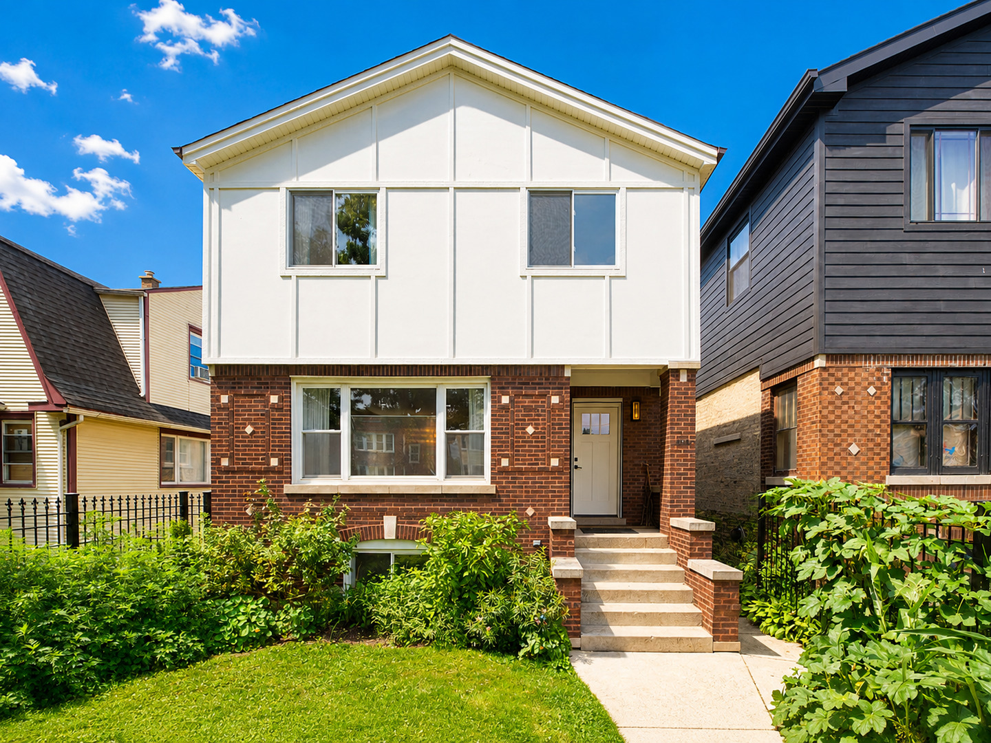 Two-story house with a white upper facade, brick lower level, and landscaped front yard.