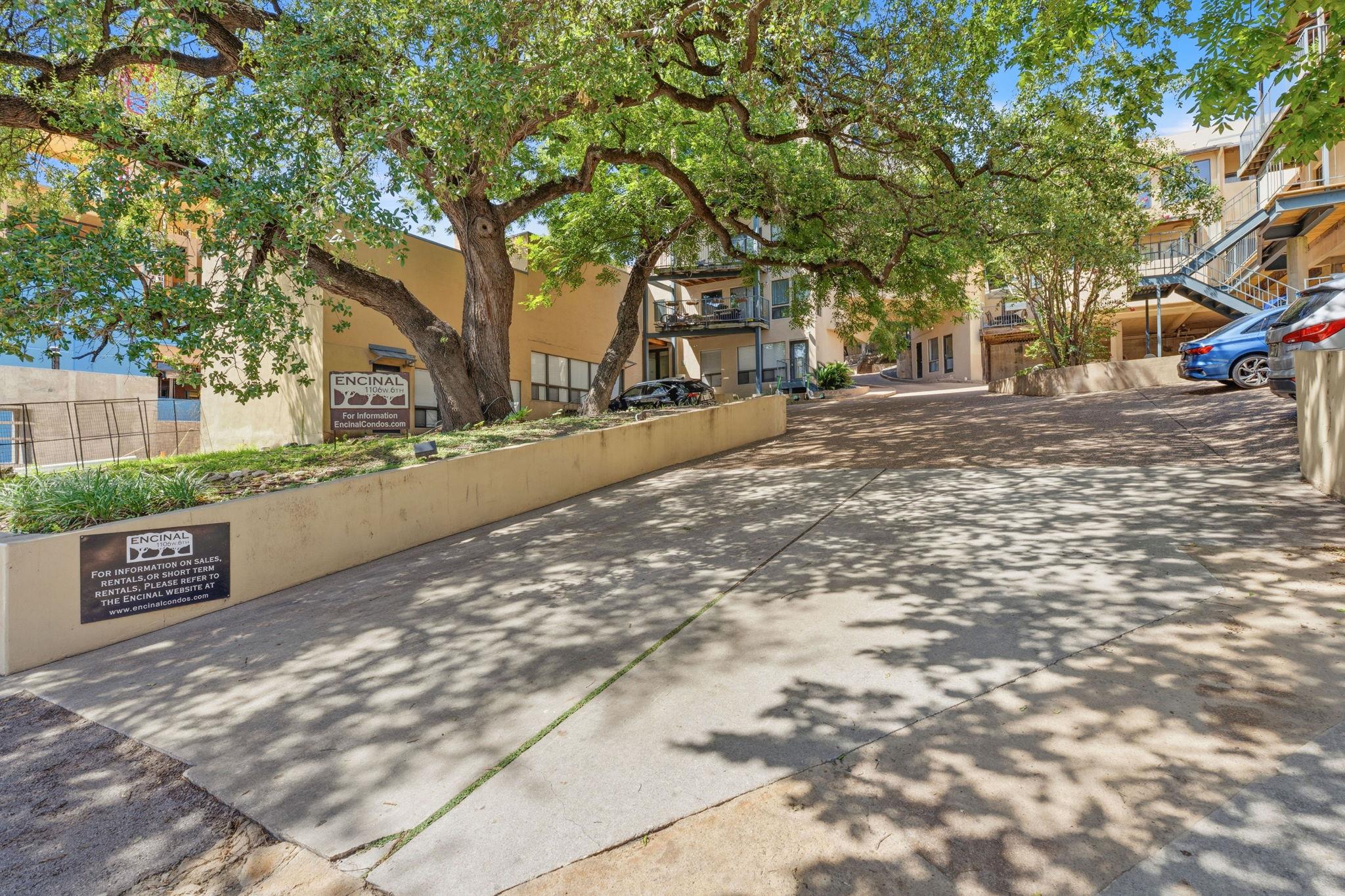Encinal condominium entrance beneath mature trees, with a shaded driveway and balconies.