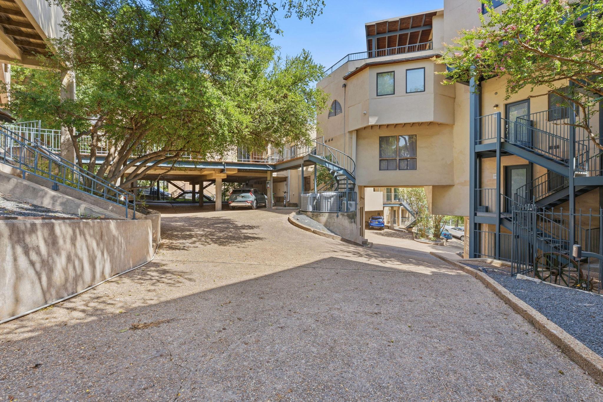 Condominium exterior with blue-gray stairways, a sloped driveway, covered parking, and mature trees.